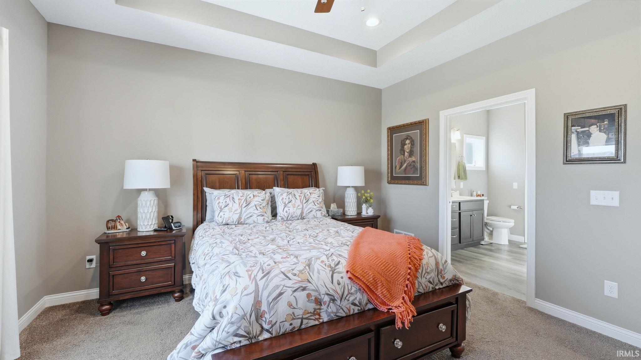 Bedroom featuring a raised ceiling, light carpet, ensuite bathroom, and ceiling fan
