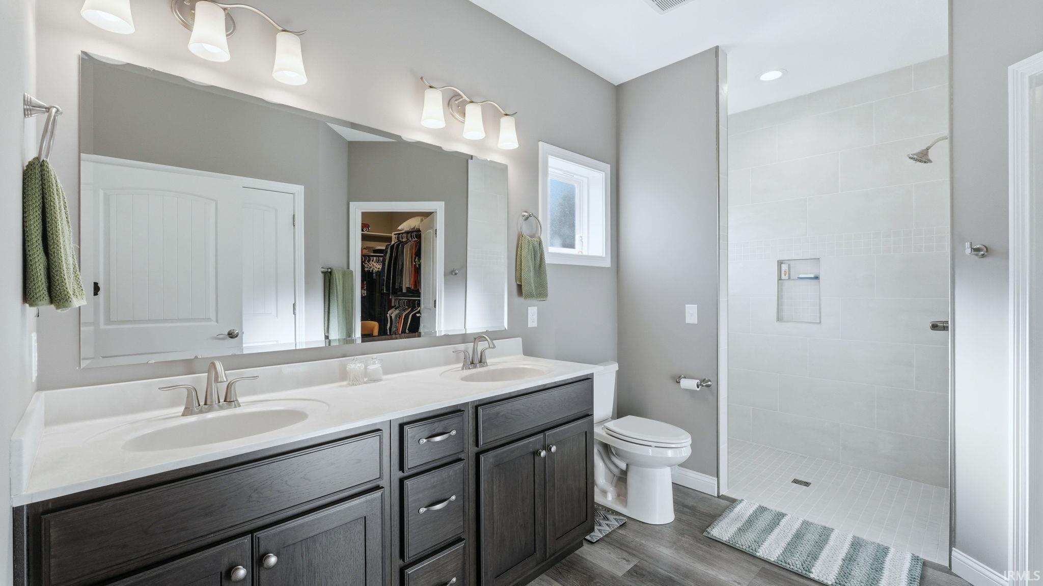 Full bath featuring double vanity, walk in shower, and dark wood-style floors