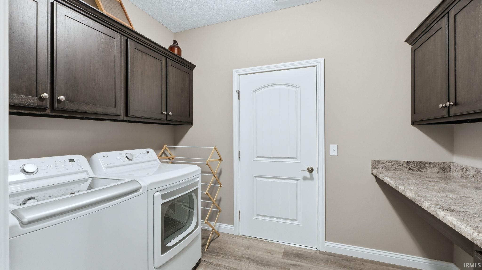 Laundry room with washing machine and clothes dryer, light wood-type flooring, and a textured ceiling