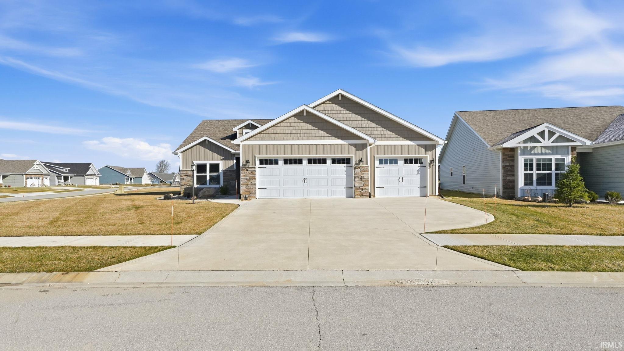 Craftsman inspired home with board and batten siding, stone siding, driveway, a front lawn, and an attached garage