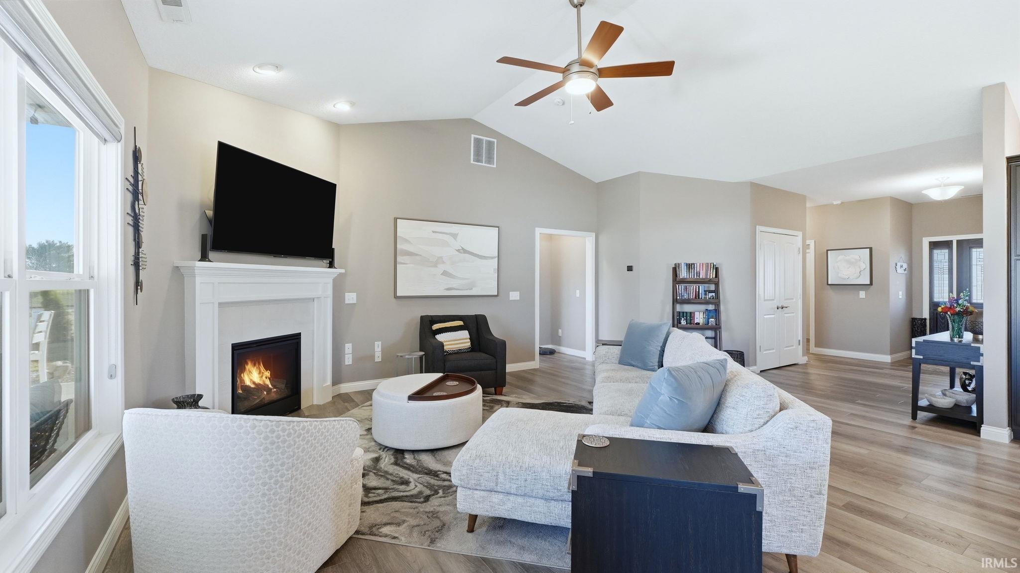Living room featuring ceiling fan, a lit fireplace, light wood finished floors, and vaulted ceiling