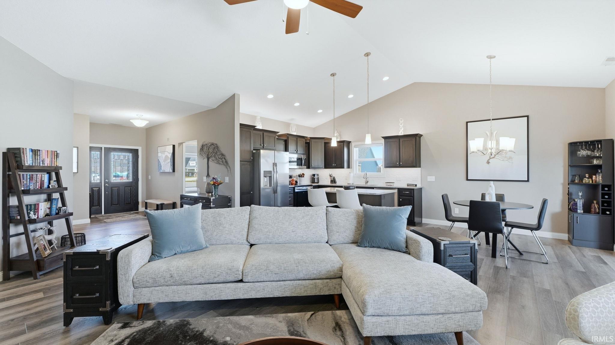 Living room featuring light wood finished floors, a chandelier, a high ceiling, healthy amount of natural light, and ceiling fan