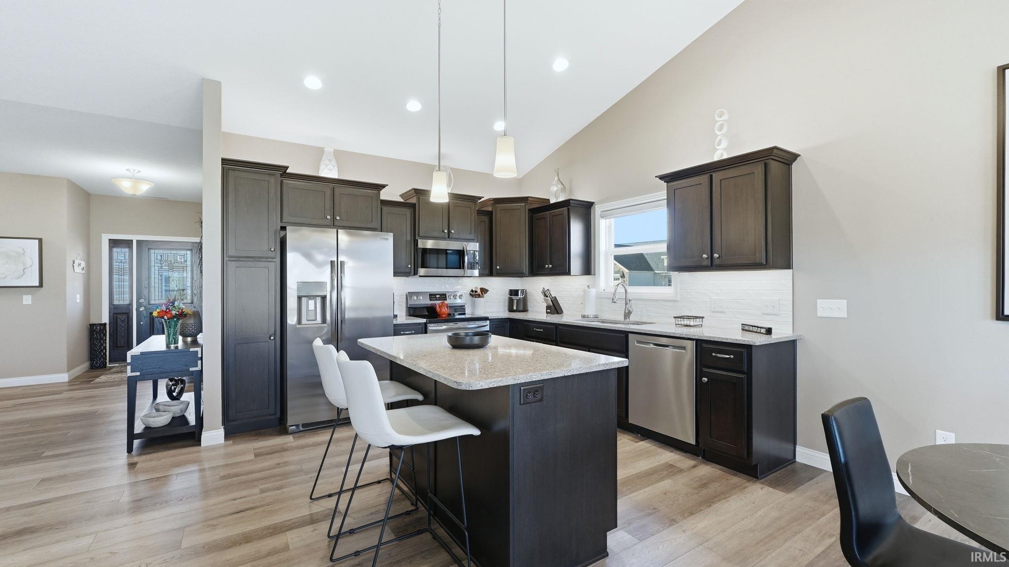 Kitchen with stainless steel appliances, a kitchen bar, decorative backsplash, light stone countertops, and a center island