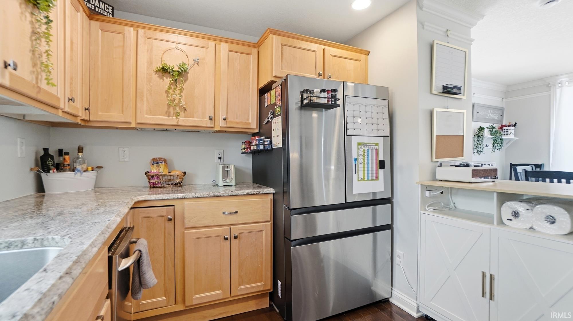 Kitchen with light wood finish cabinets, stainless steel appliances, dark wood-type flooring, and light stone countertops