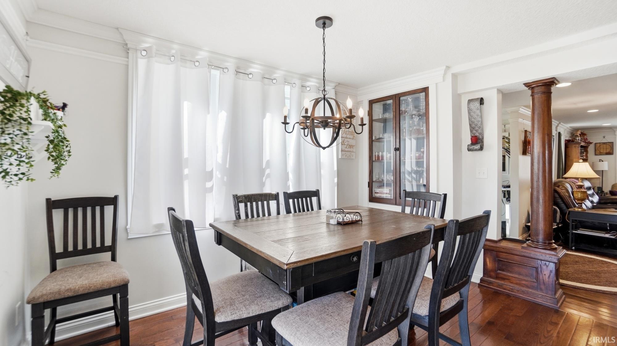 Dining area with ornate columns, crown molding, dark wood-style flooring, and suspended lighting