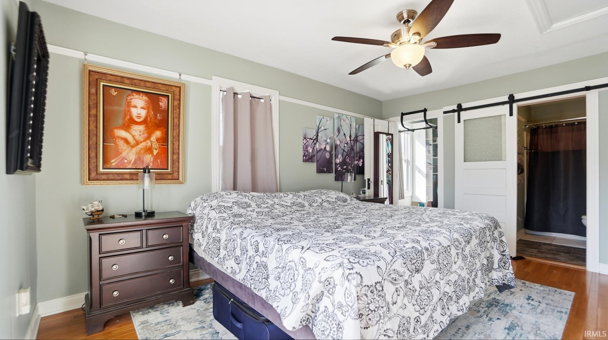 Bedroom with a barn door, wood finished floors, and ceiling fan