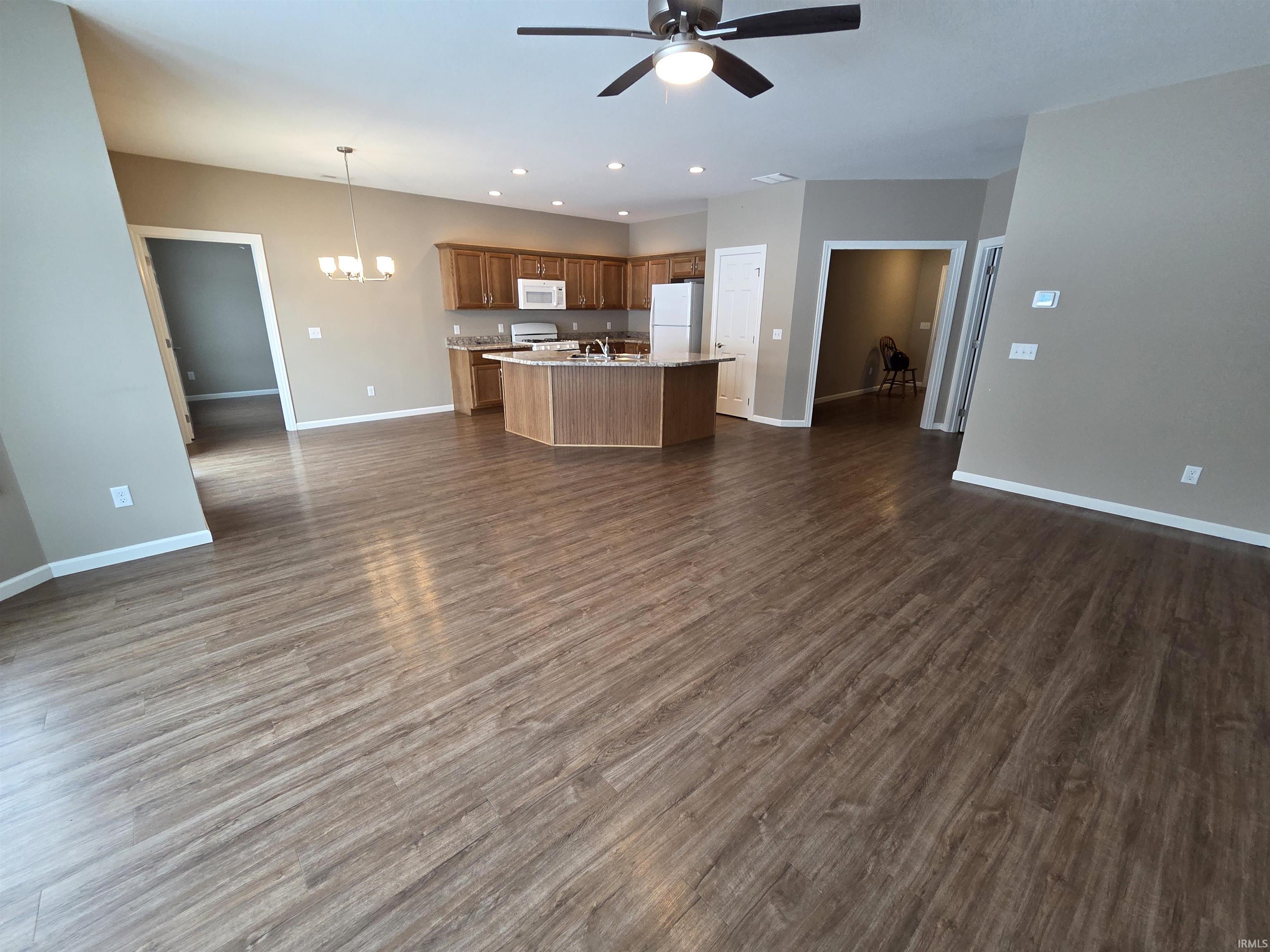 Kitchen with open floor plan, ceiling fan, a center island with sink, white appliances, and dark wood-style floors