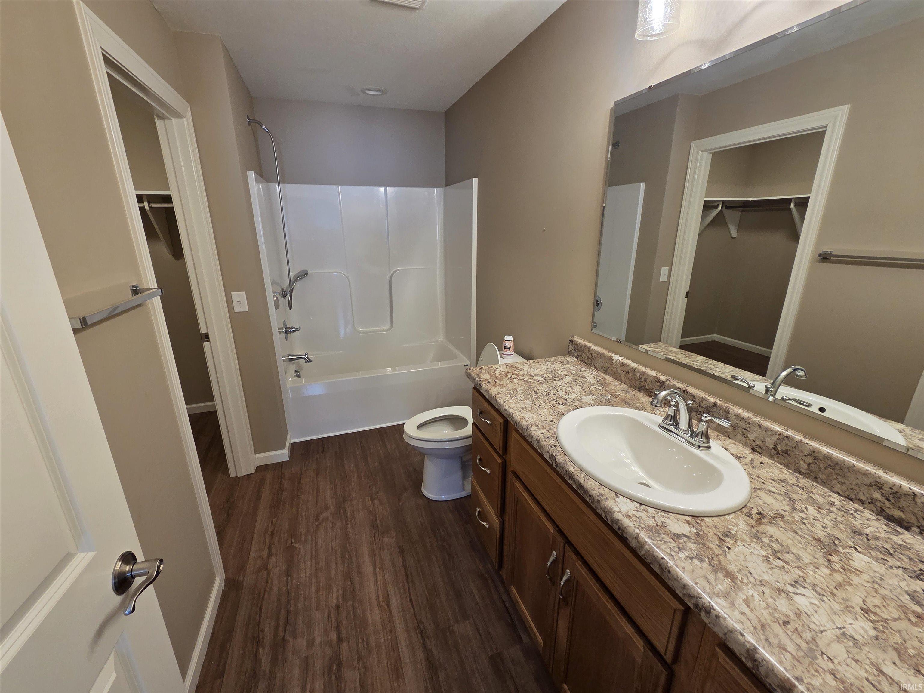 Bathroom with a spacious closet, vanity,  shower combination, and dark wood-type flooring