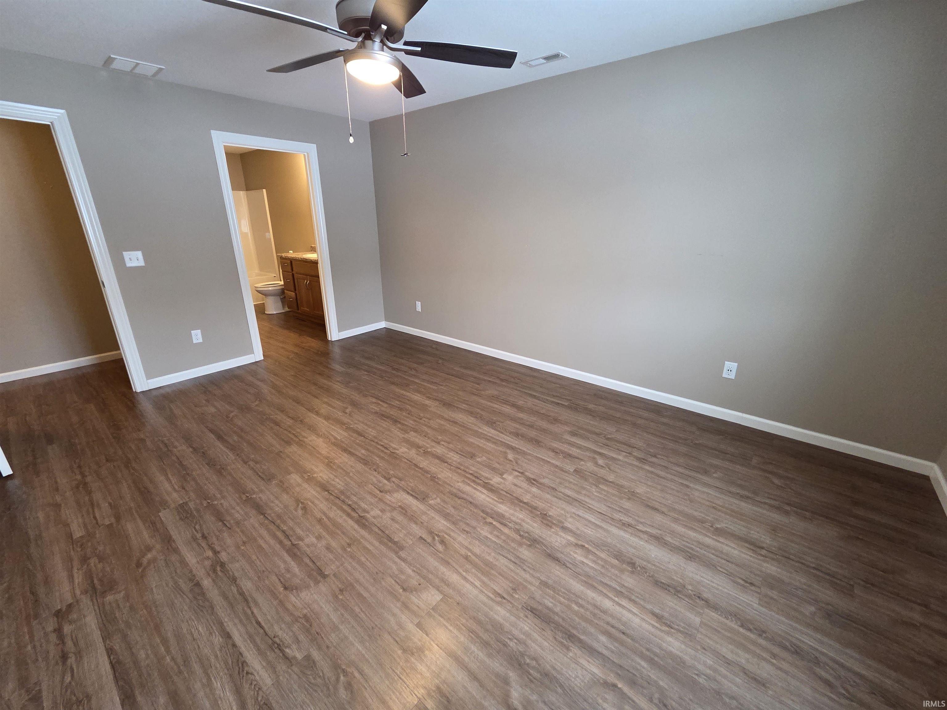 Unfurnished bedroom with ensuite bath, ceiling fan, and dark wood-style flooring