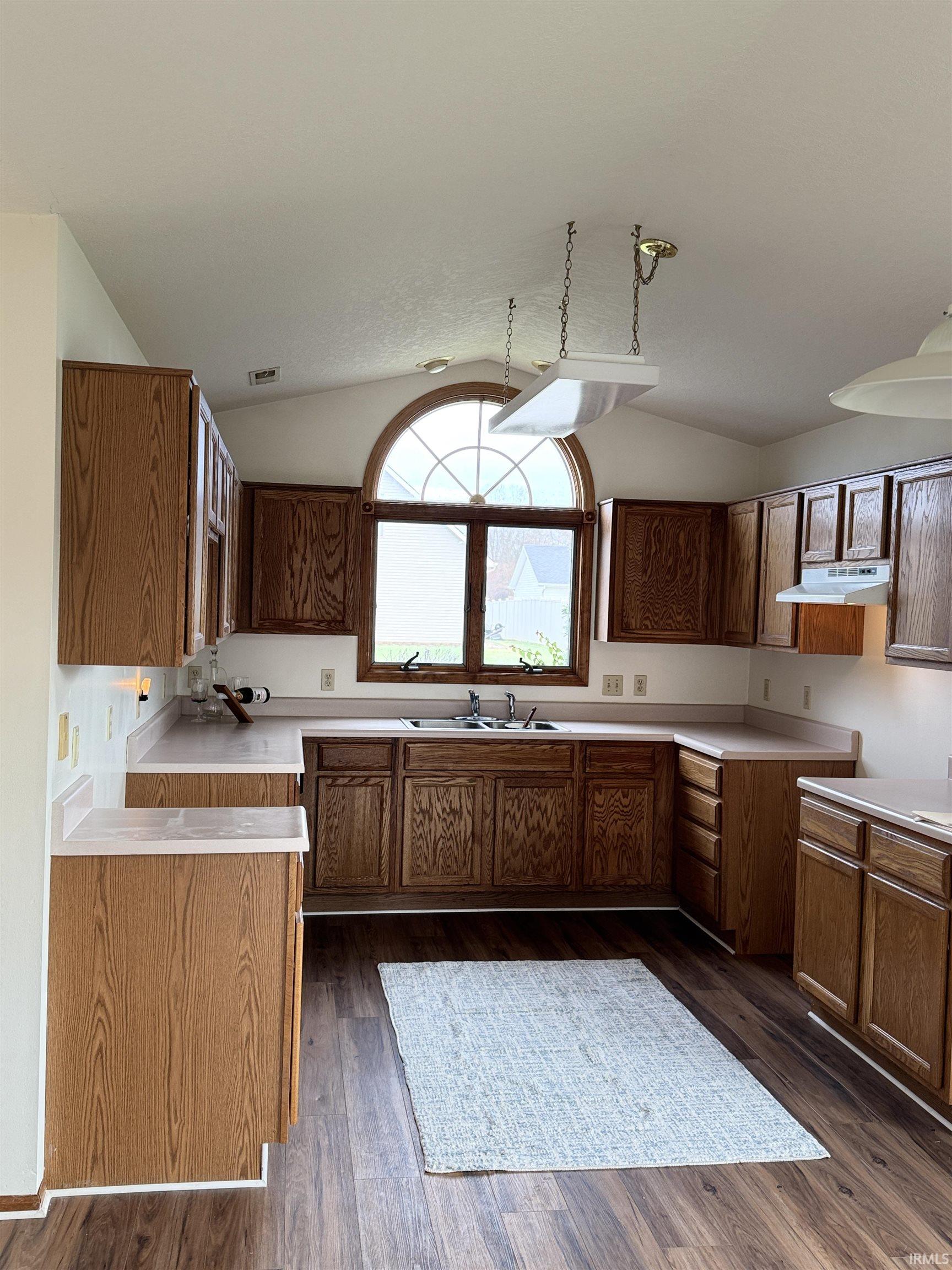 Kitchen with light countertops, wood finish cabinets, dark wood-style floors, and vaulted ceiling
