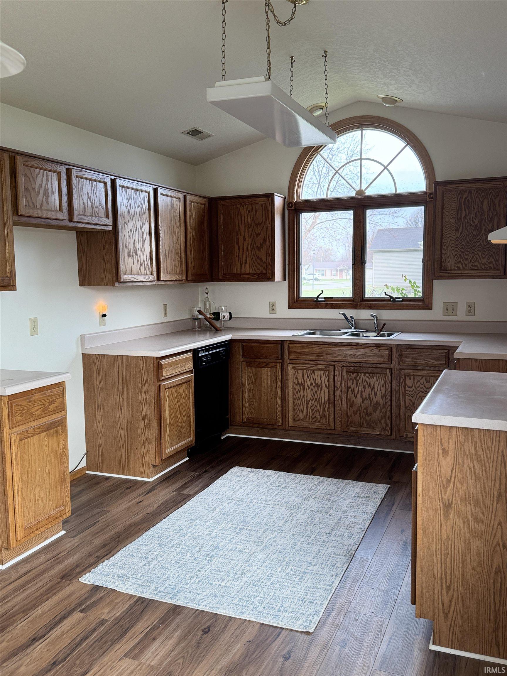 Kitchen with light countertops, vaulted ceiling, dark wood-style floors, black dishwasher, and wood finish cabinets