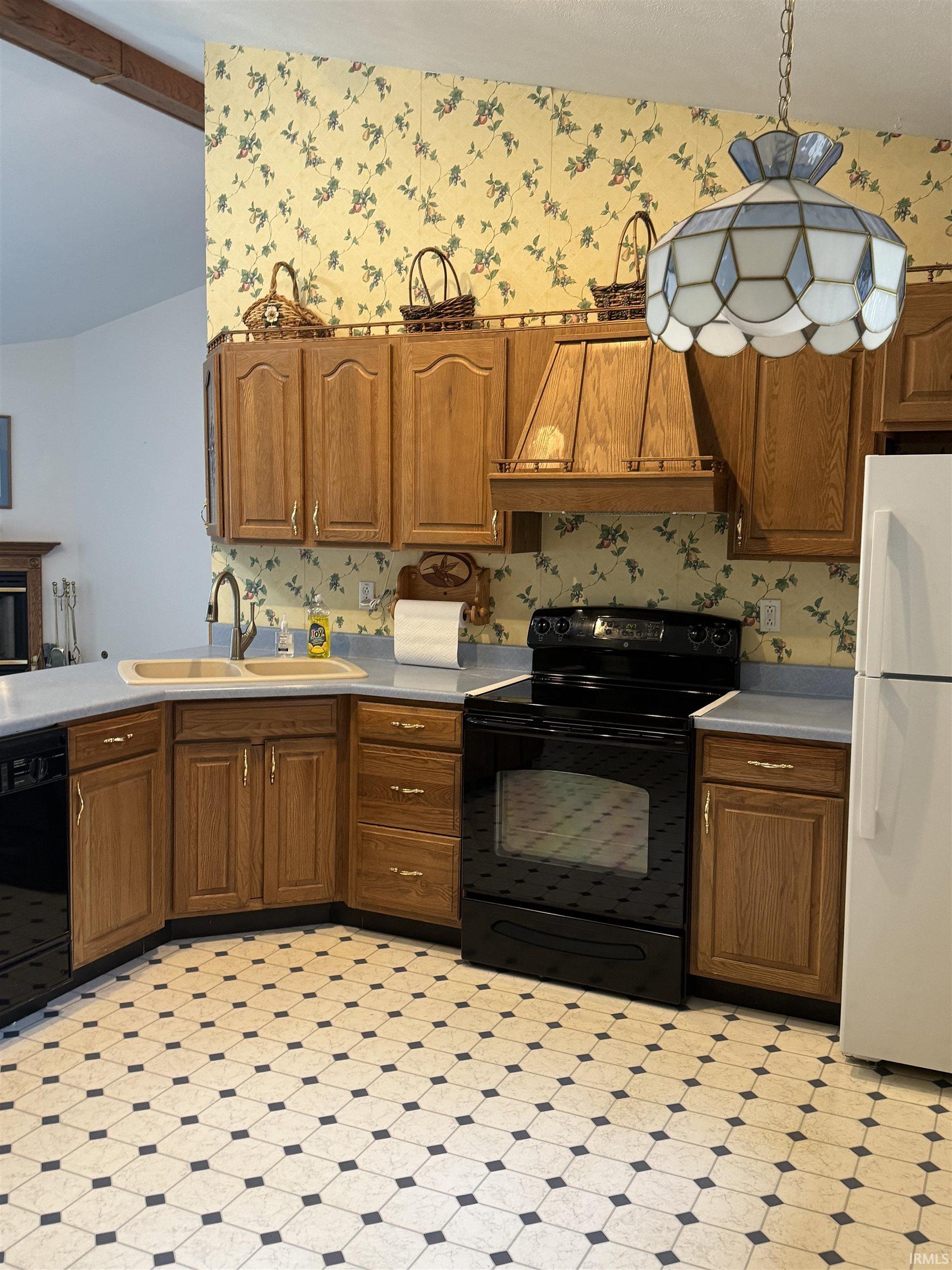 Kitchen with black appliances, wood finish cabinets, light countertops, light floors, and wallpapered walls