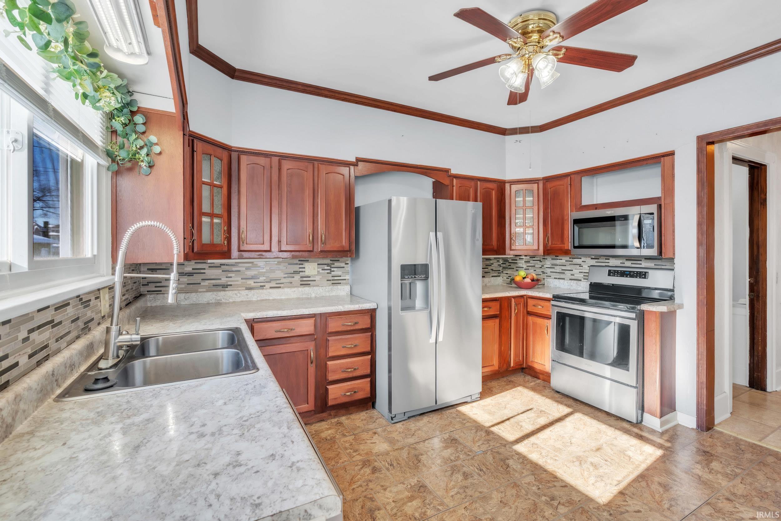 Kitchen with glass fronted cabinets, stainless steel appliances, light countertops, crown molding, and a ceiling fan