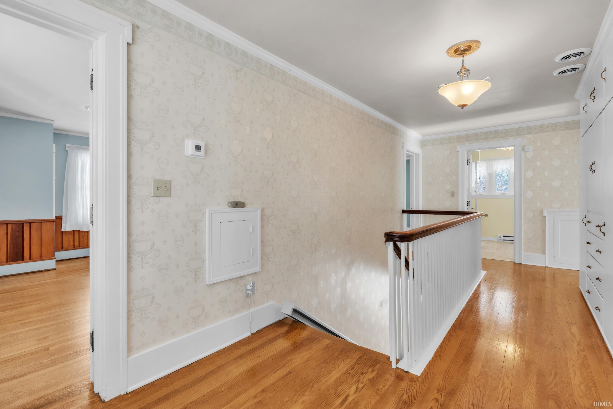 Hallway featuring an upstairs landing, light wood-type flooring, ornamental molding, and wallpapered walls