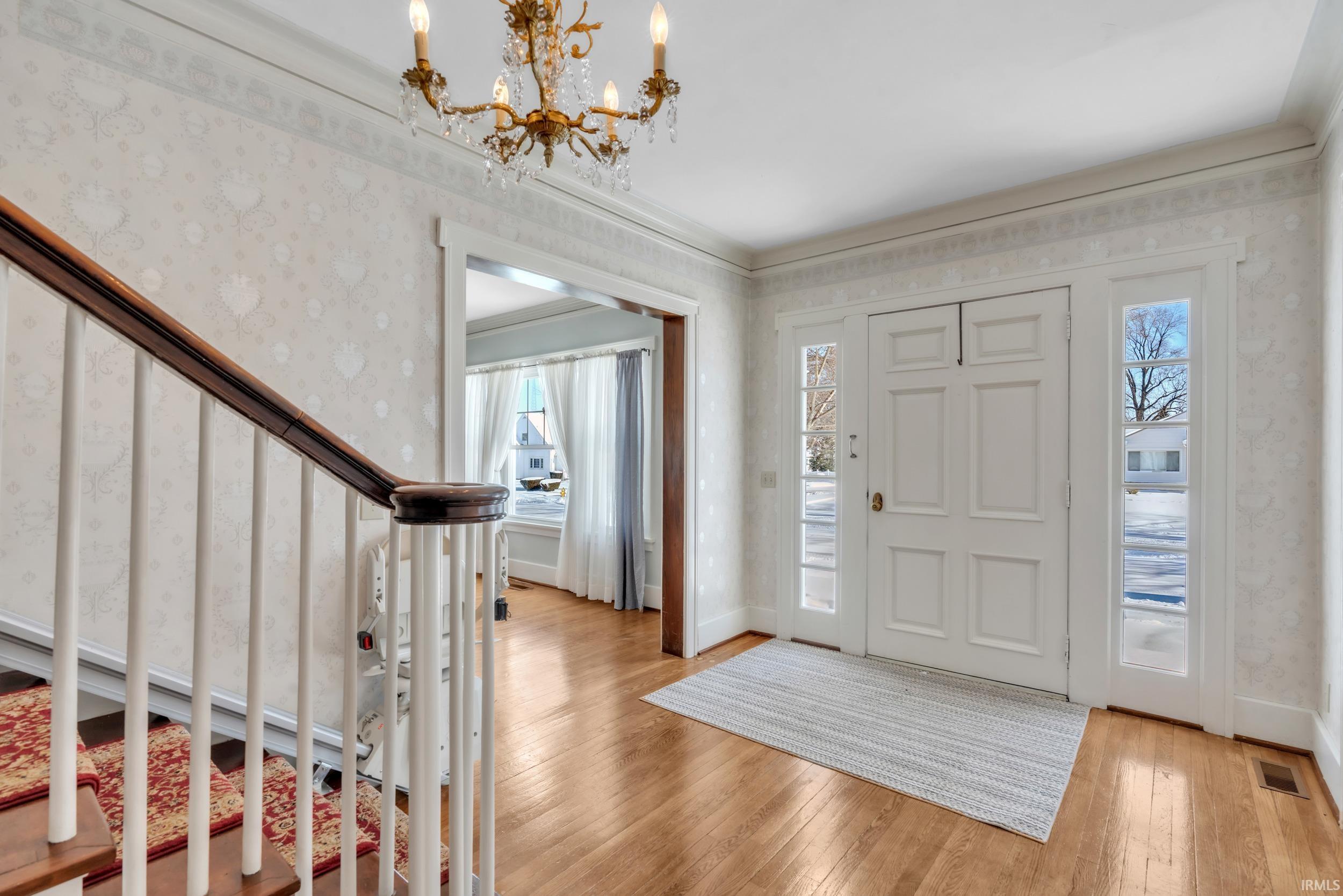 Foyer entrance with wallpapered walls, light wood finished floors, a chandelier, and crown molding