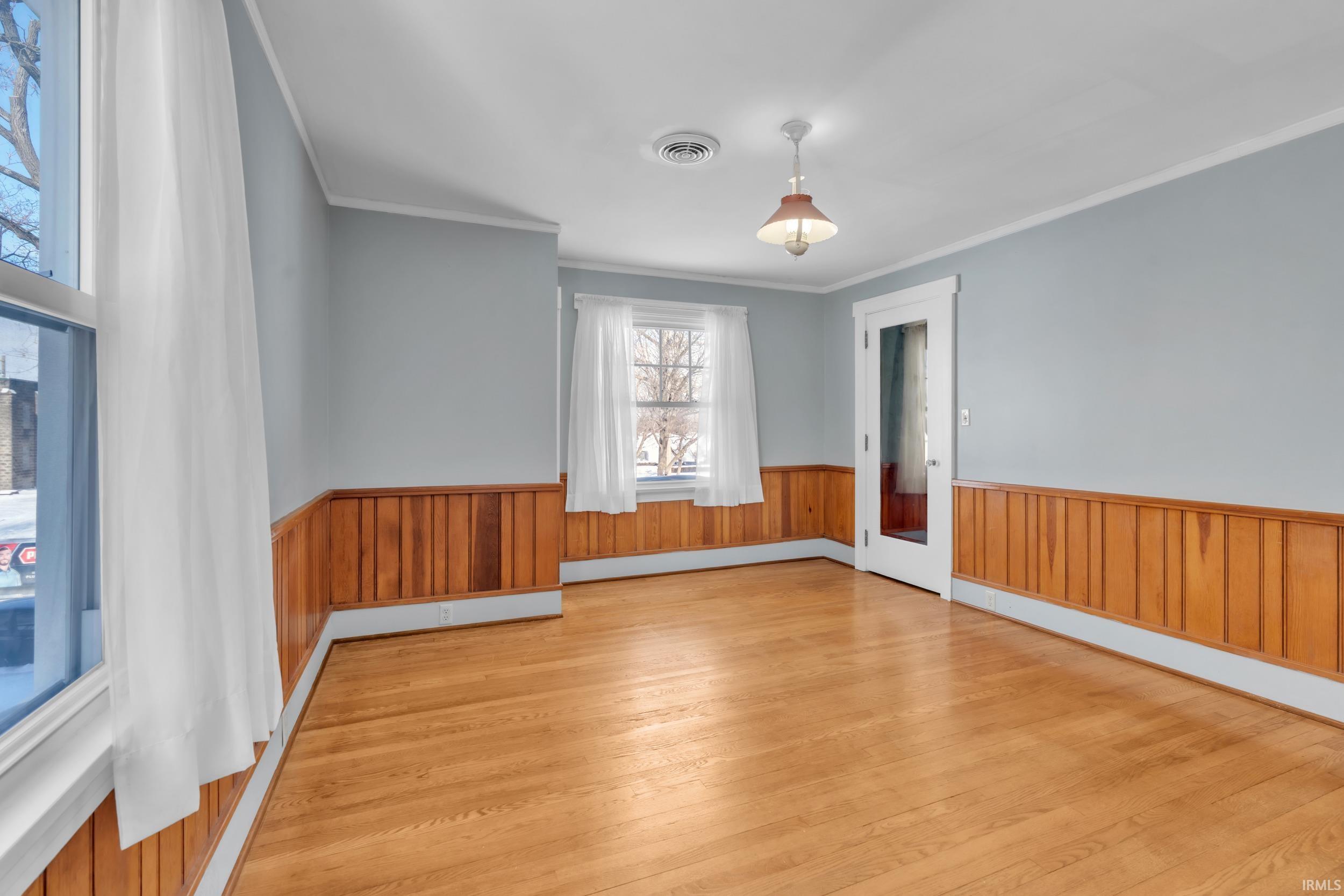 Spare room featuring a wainscoted wall, light wood-type flooring, ornamental molding, a baseboard heating unit, and wooden walls