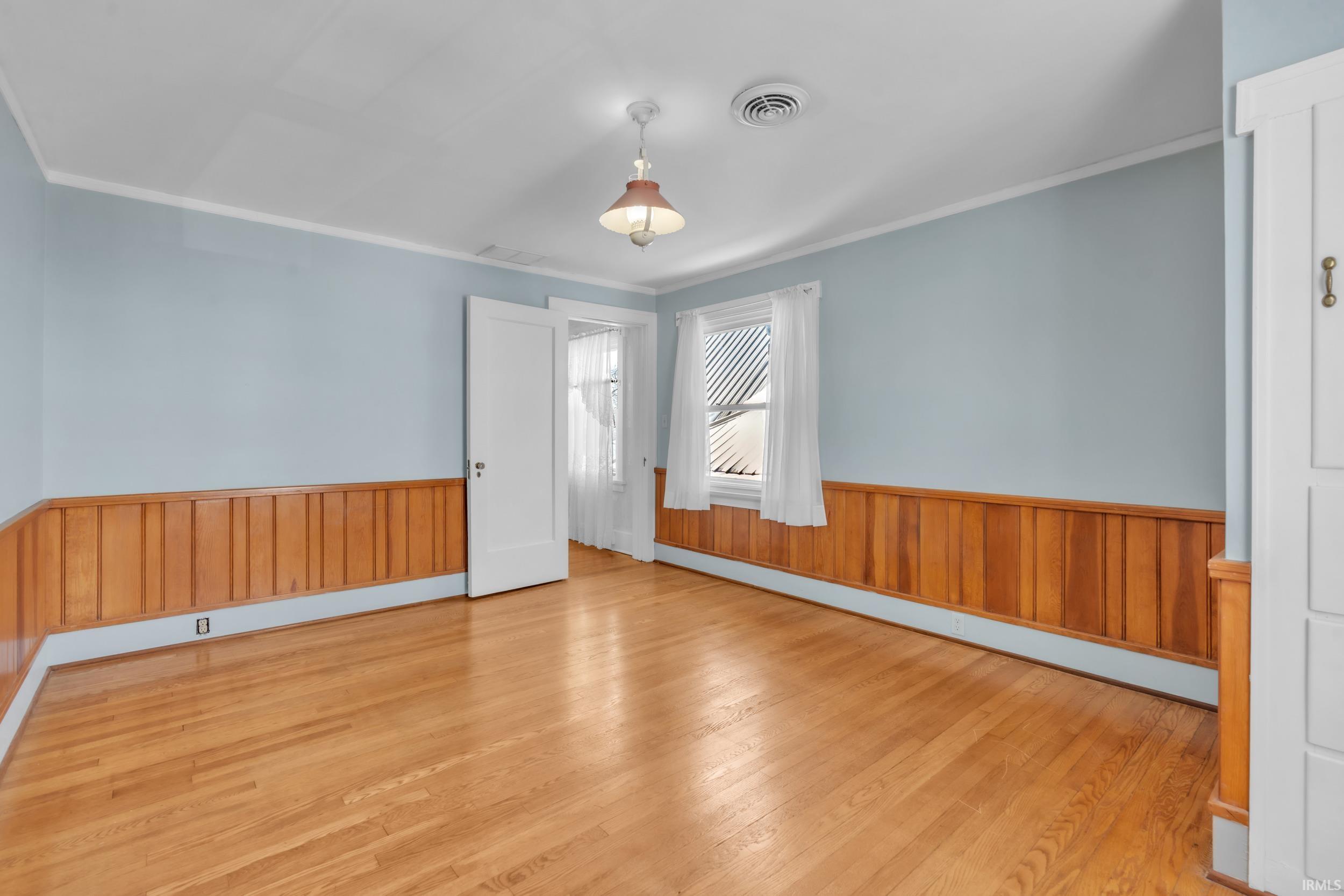 Unfurnished room with wainscoting, wood walls, a baseboard radiator, light wood-type flooring, and crown molding