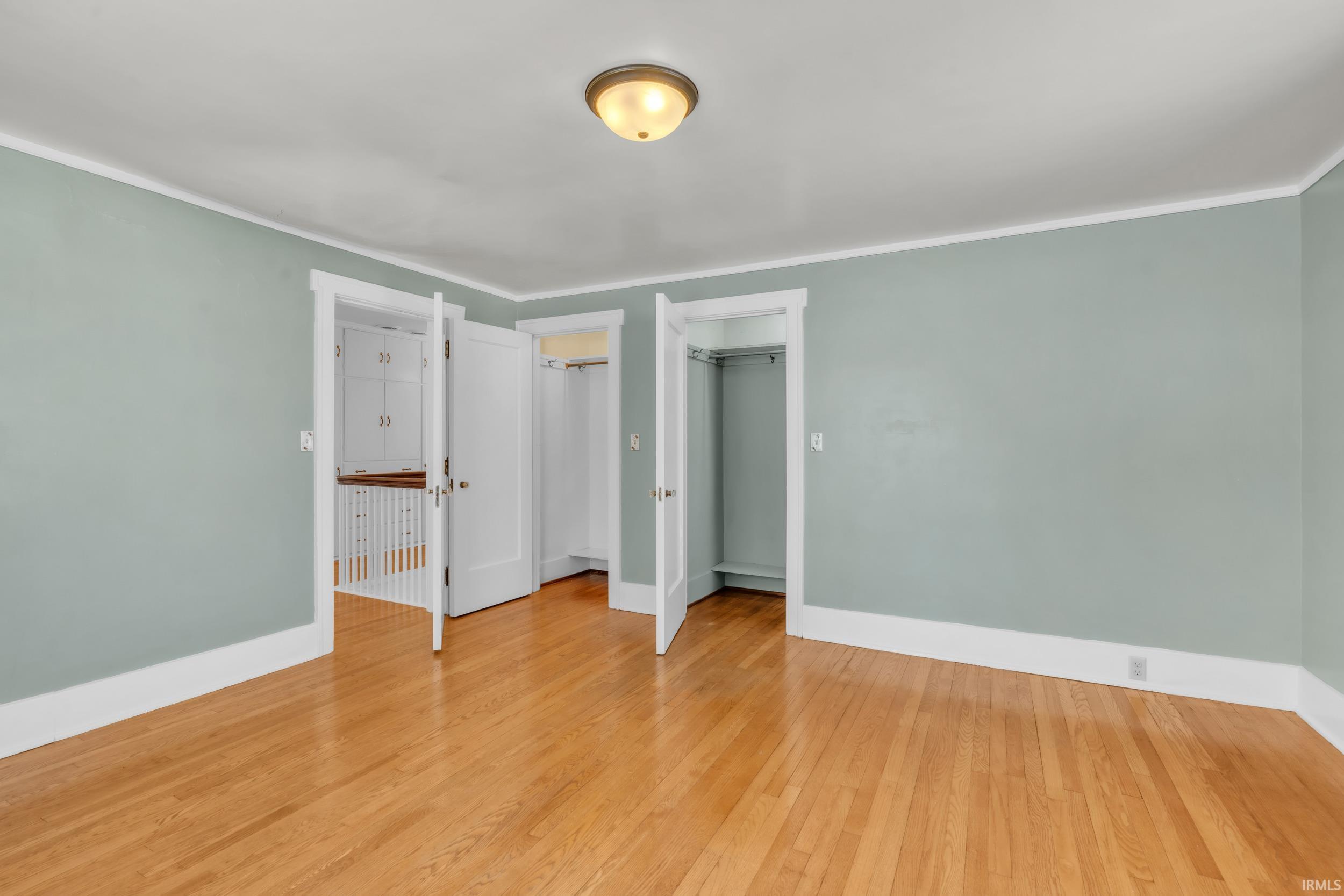 Unfurnished bedroom with two closets, light wood-style flooring, and ornamental molding