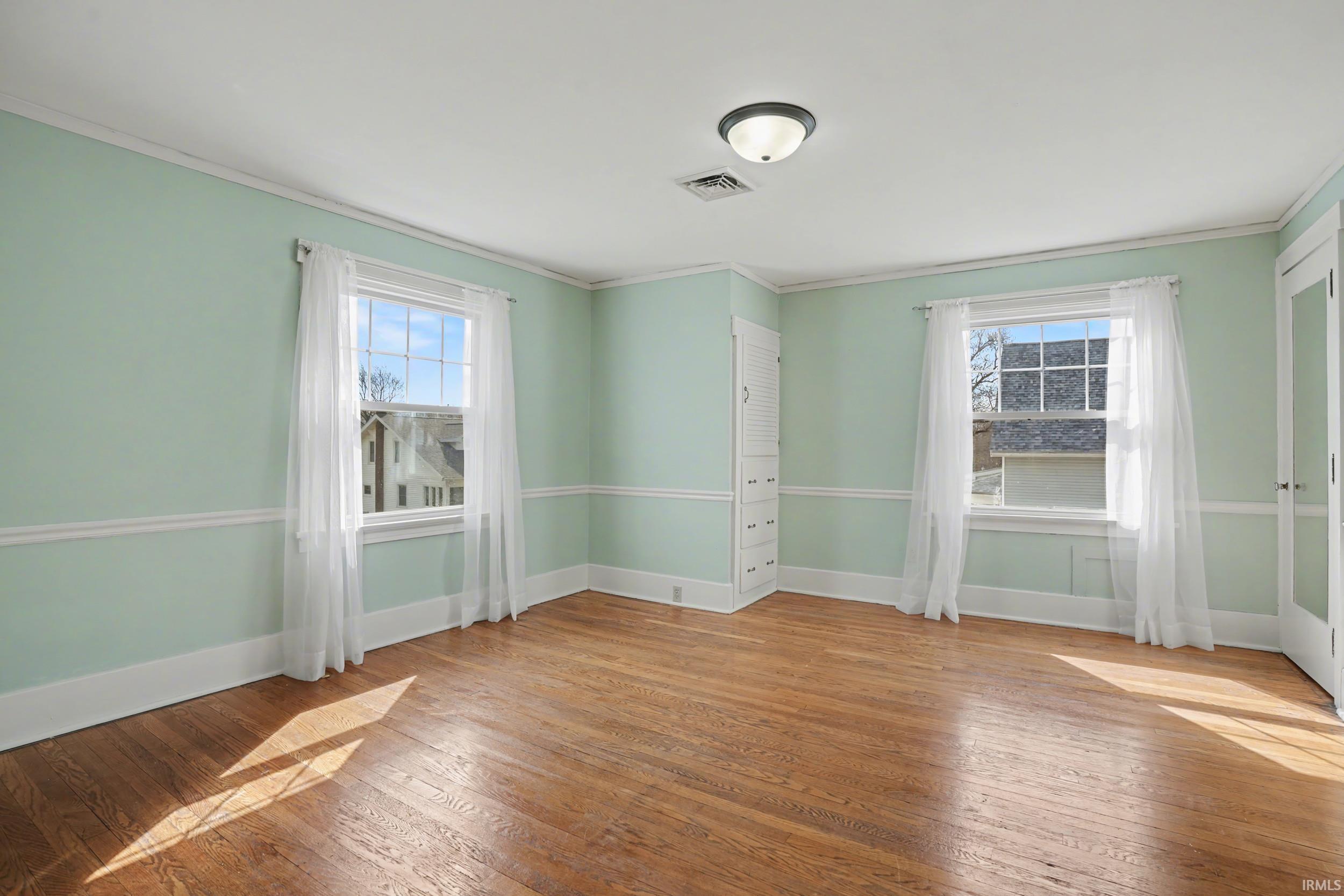 Empty room with light wood-type flooring, healthy amount of natural light, and ornamental molding