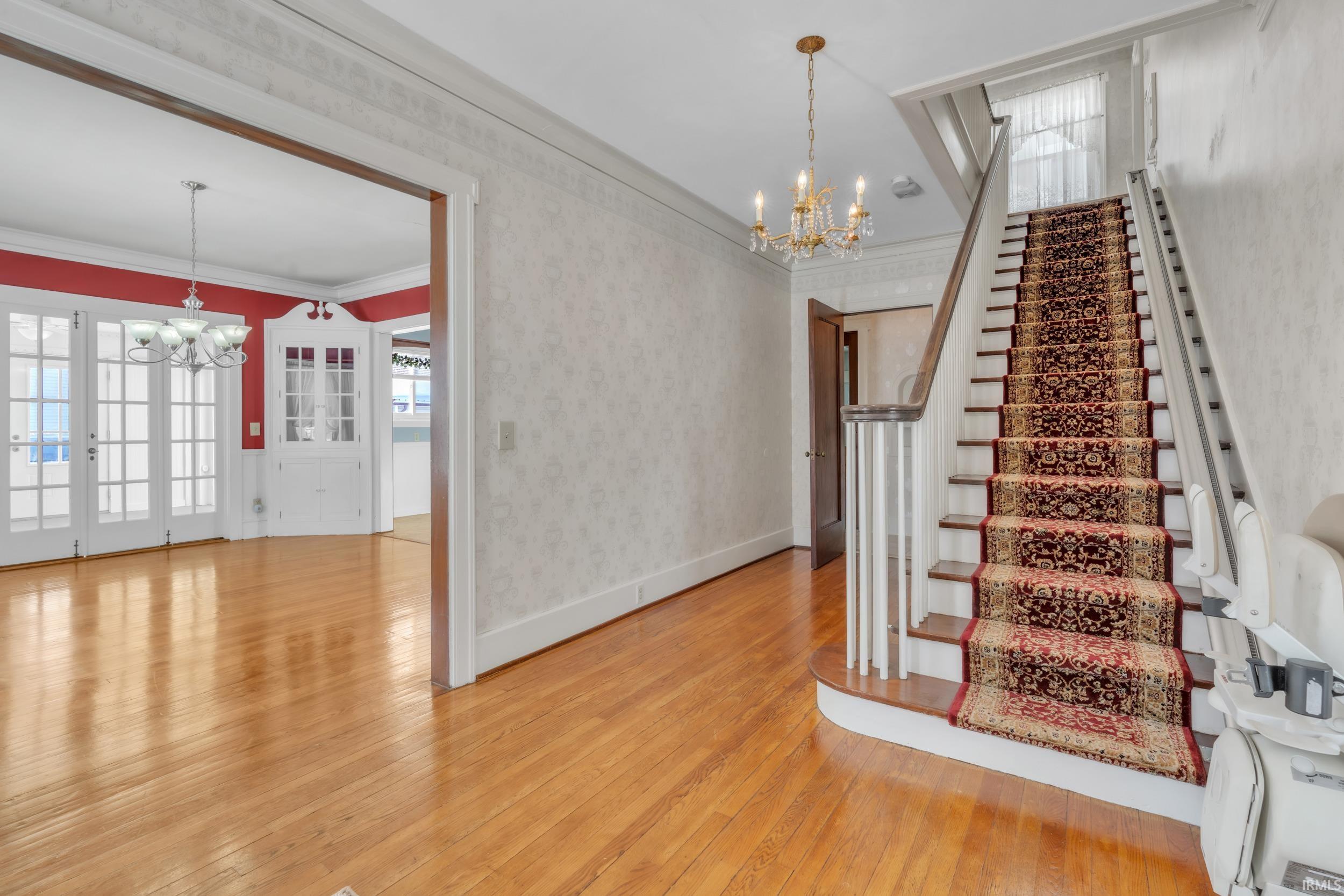 Stairway with a chandelier, wallpapered walls, plenty of natural light, hardwood / wood-style floors, and crown molding