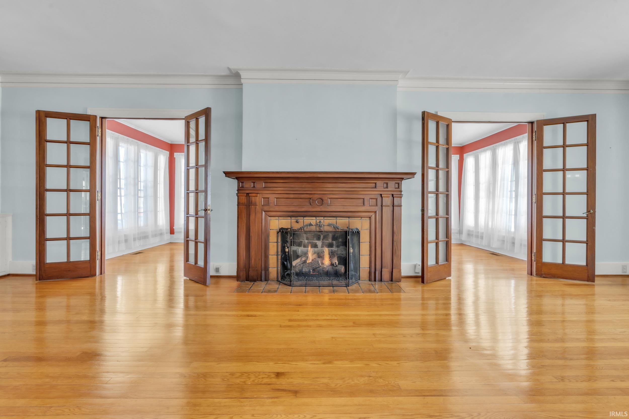 Unfurnished living room featuring french doors, light wood finished floors, ornamental molding, and a fireplace