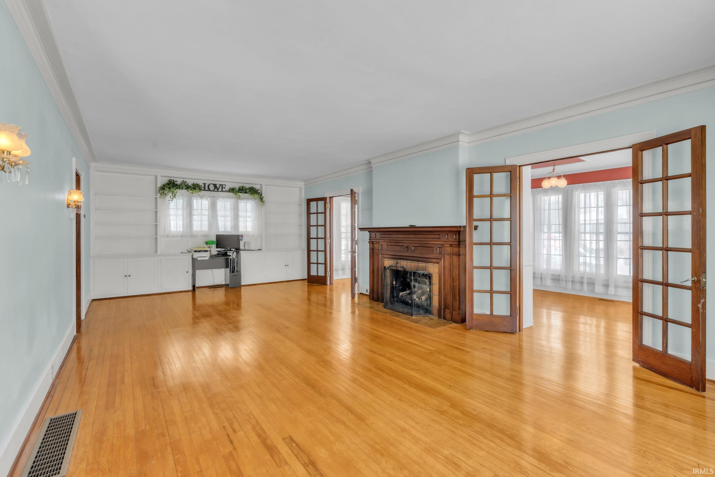 Unfurnished living room with french doors, light wood-style flooring, a fireplace with flush hearth, and crown molding