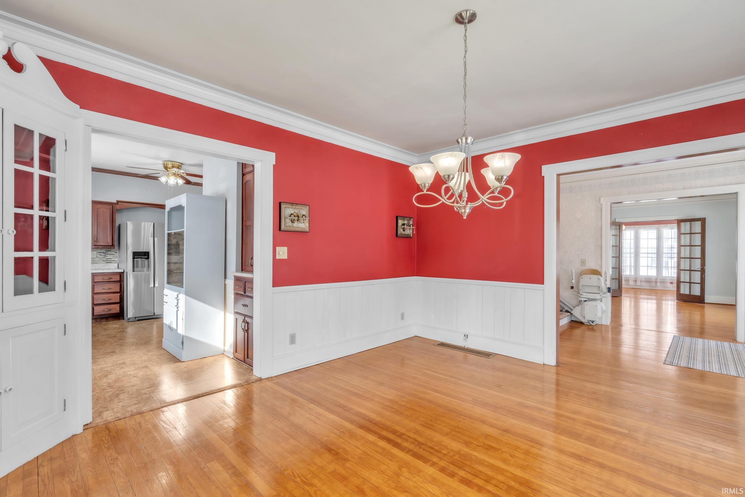 Unfurnished dining area with ceiling fan, light wood-style flooring, suspended lighting, crown molding, and a wainscoted wall