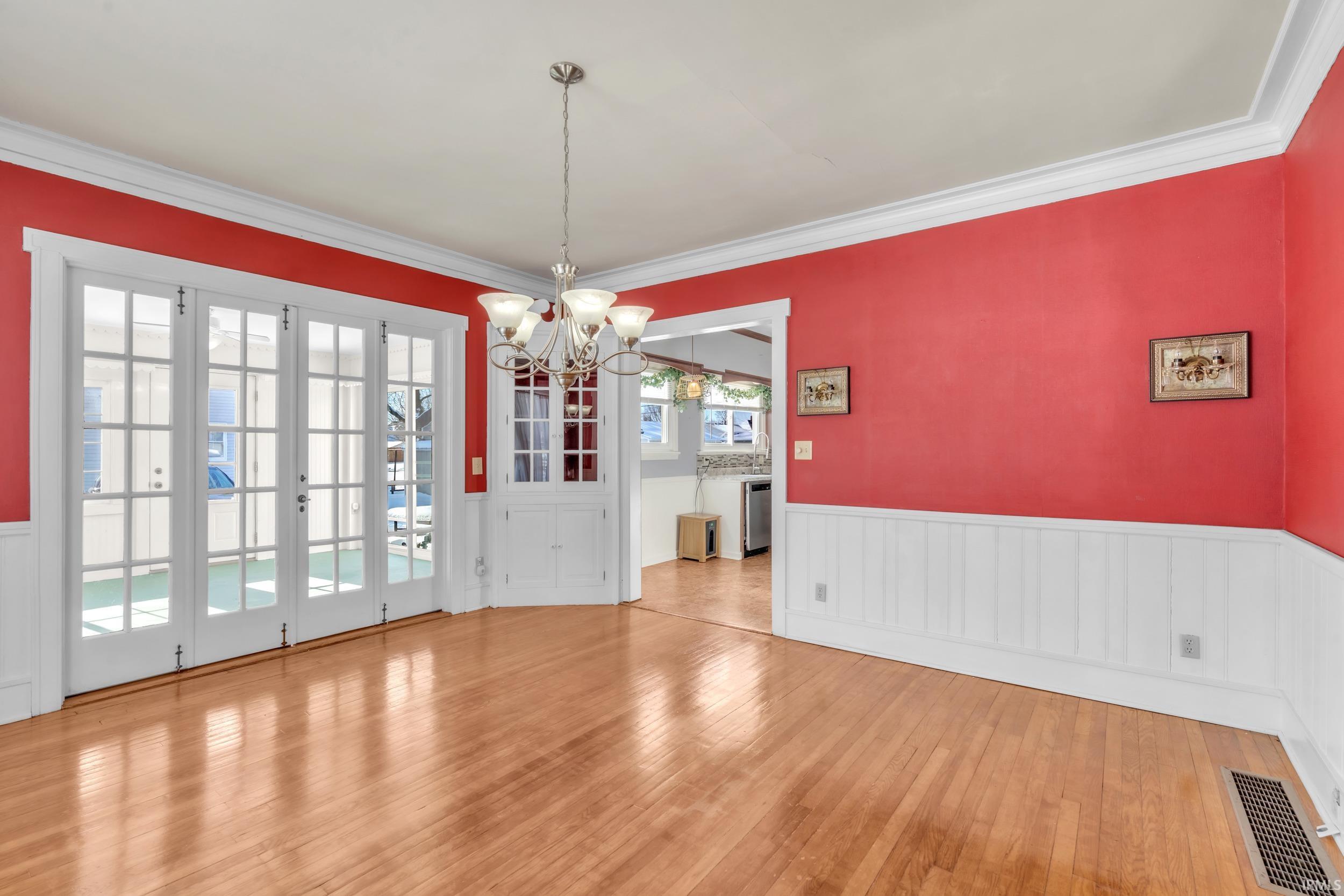 Unfurnished dining area featuring wainscoting, suspended lighting, light wood-style flooring, crown molding, and a decorative wall