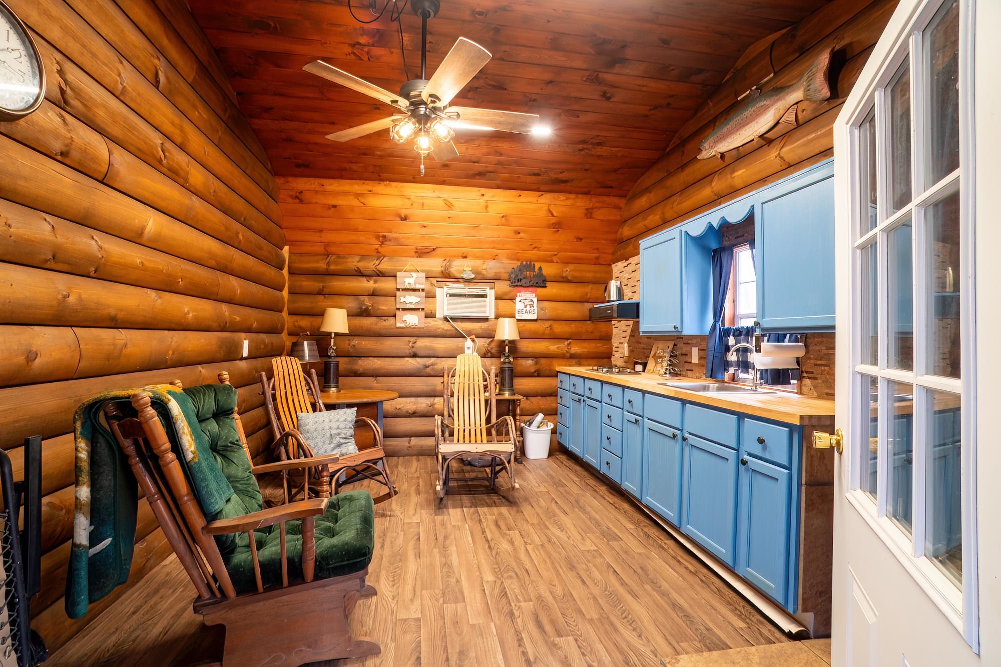 Living area with log walls, light wood-style flooring, a ceiling fan, and a vaulted wood ceiling