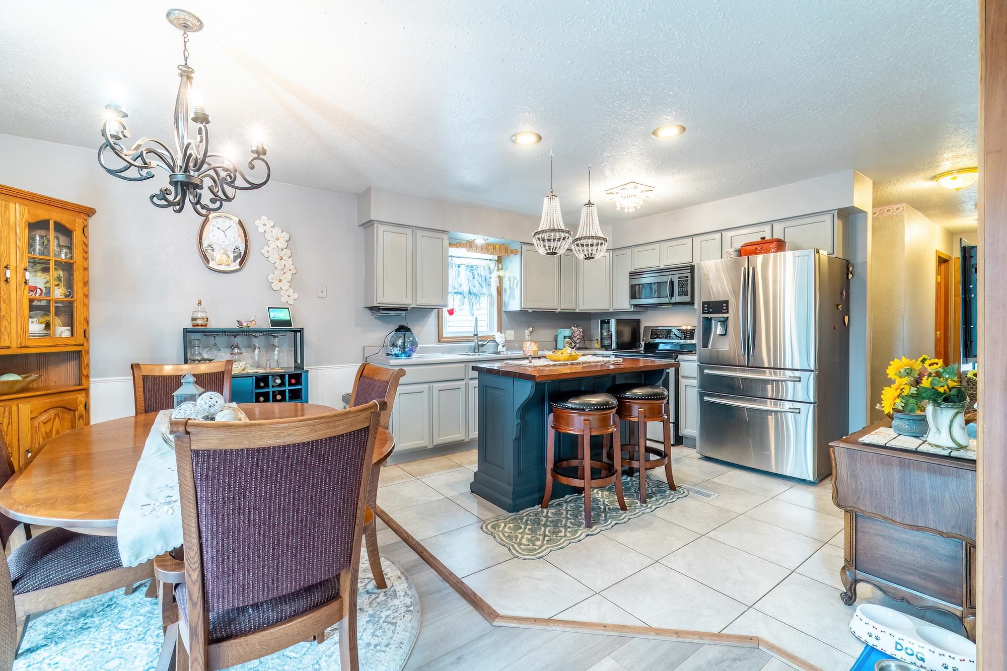Kitchen featuring a chandelier, stainless steel appliances, gray cabinets, a kitchen island, and a wainscoted wall
