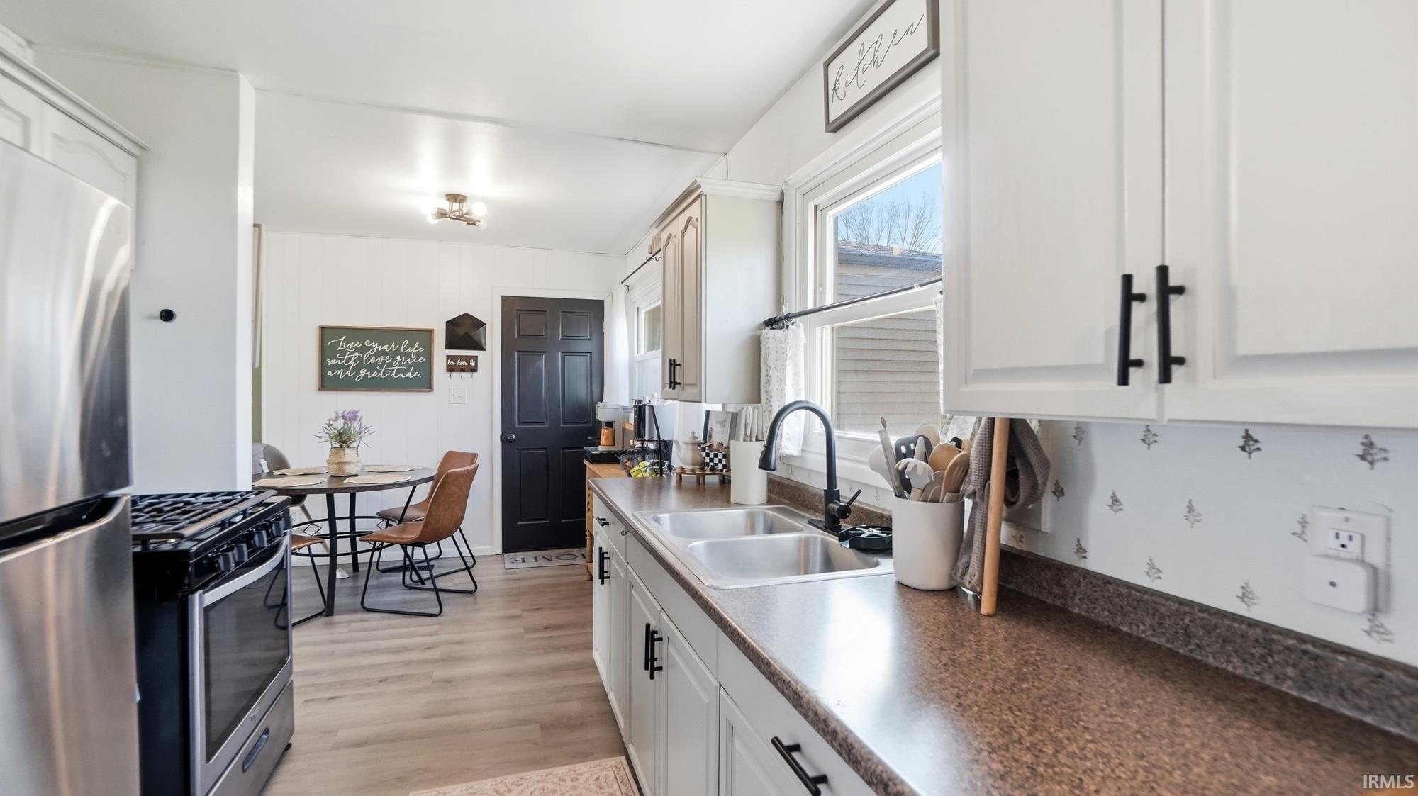 Kitchen with stainless steel appliances, white cabinetry, dark countertops, and light wood finished floors