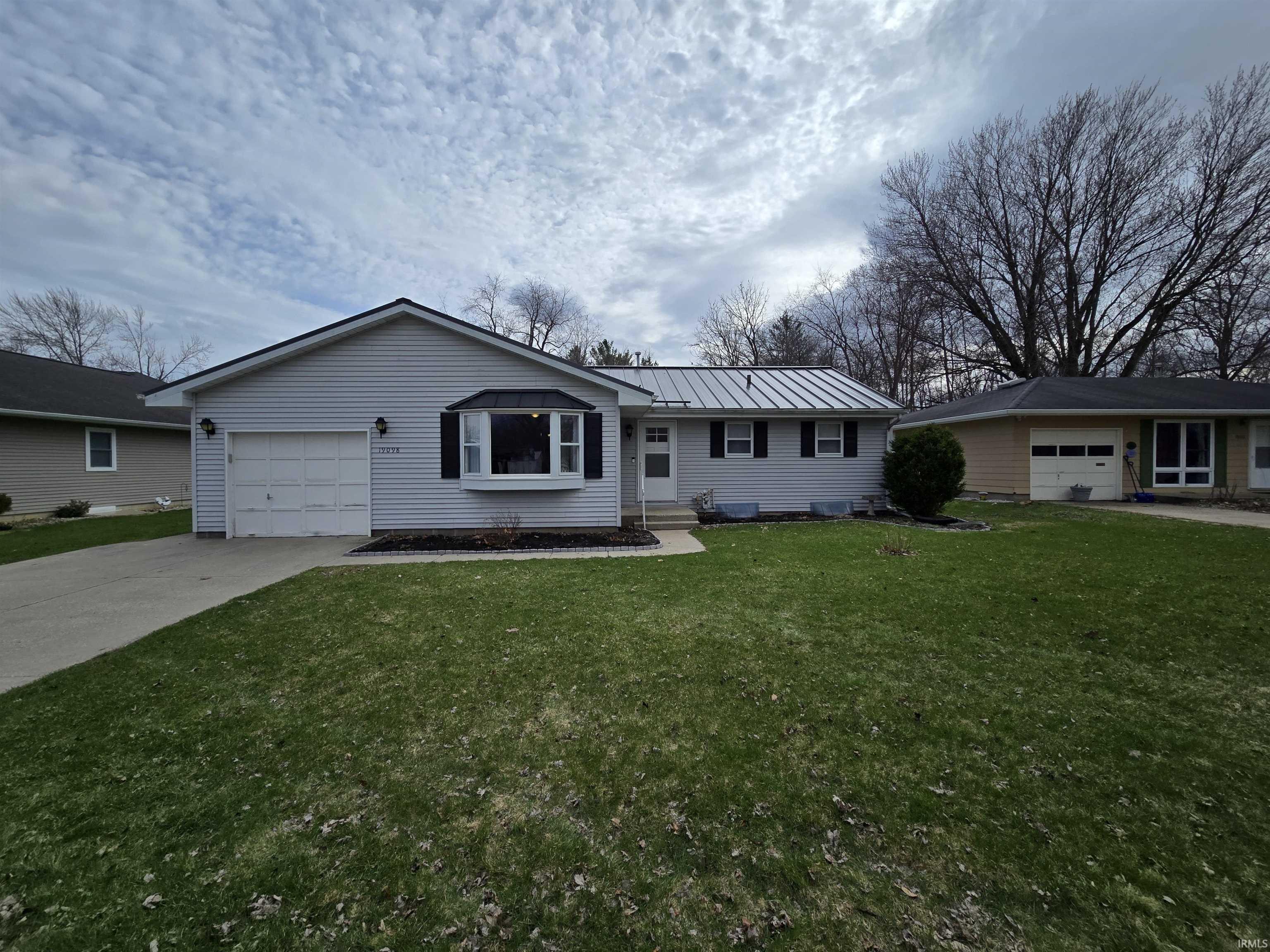 Single story home with a front yard, a standing seam roof, an attached garage, and concrete driveway