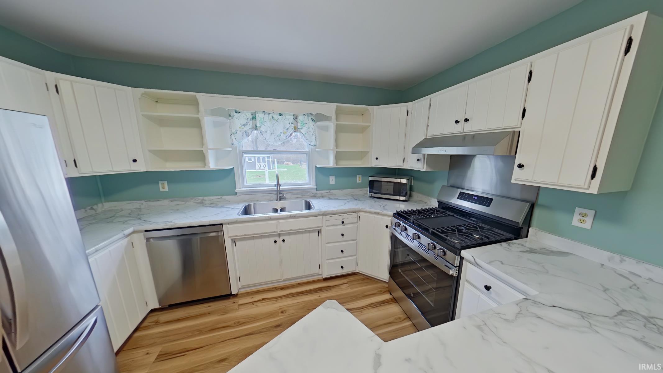 Kitchen featuring stainless steel appliances, white cabinets, light wood finished floors, light stone counters, and open shelves