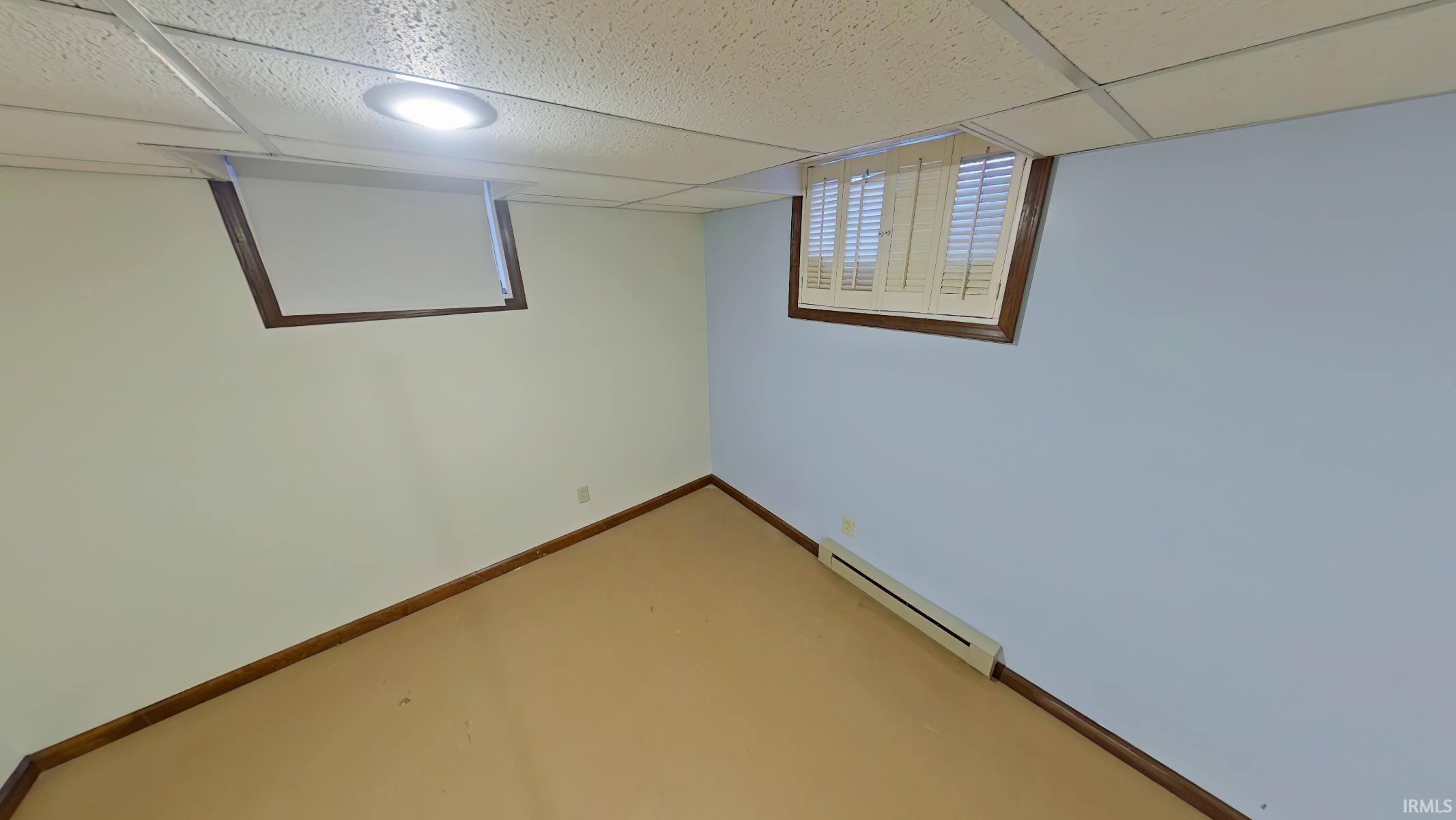 Finished basement with a baseboard radiator and a paneled ceiling