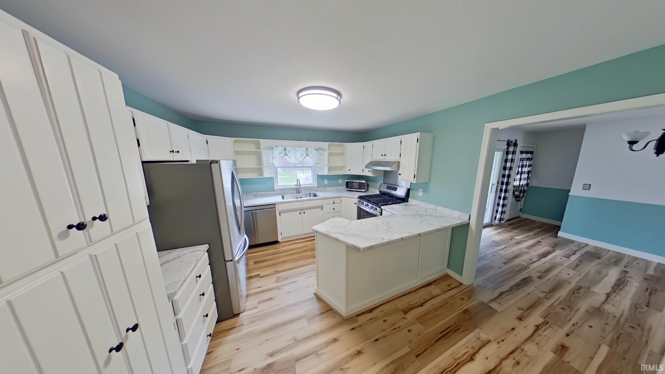 Kitchen featuring stainless steel appliances, light wood finished floors, a peninsula, and white cabinets