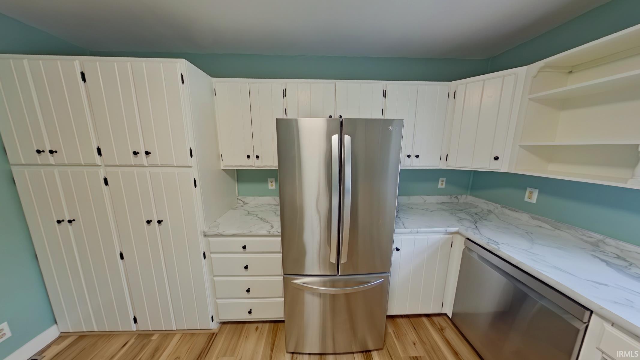 Kitchen with open shelves, stainless steel appliances, white cabinets, light wood-style floors, and light stone countertops