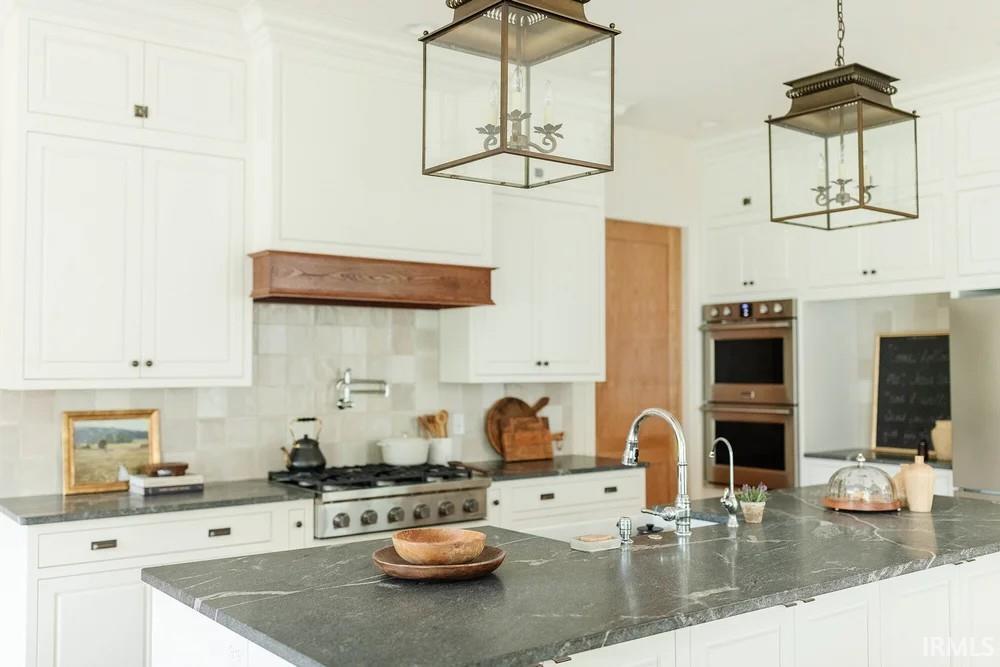 Kitchen featuring white cabinets, dark stone countertops, stainless steel appliances, and tasteful backsplash