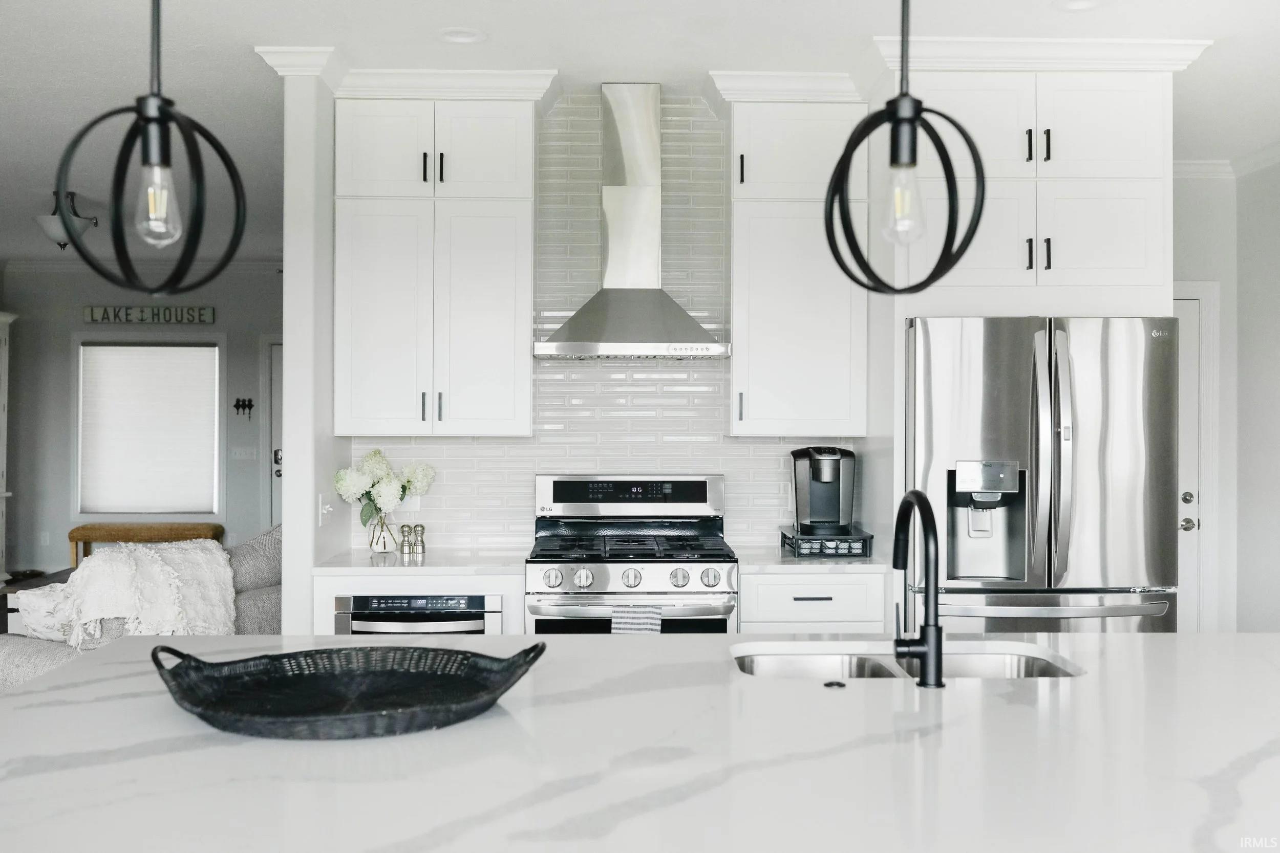 Kitchen featuring stainless steel appliances, white cabinets, light stone countertops, pendant lighting, and tasteful backsplash
