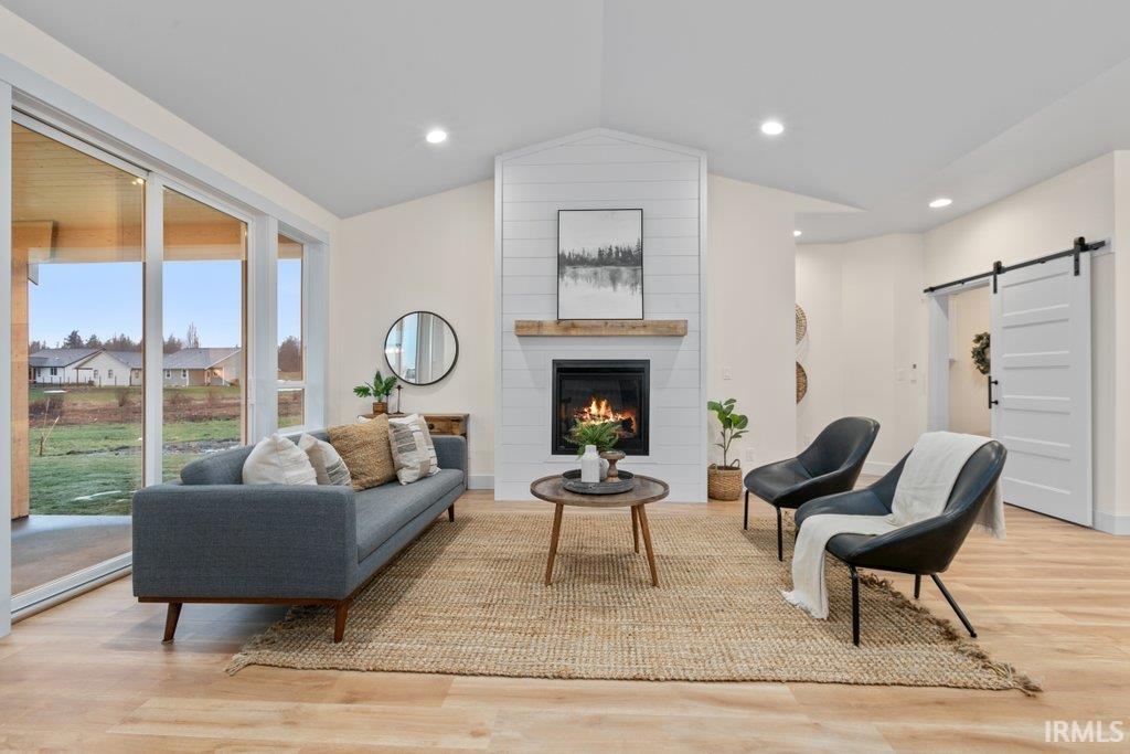Living room featuring a barn door, light wood-type flooring, a large fireplace, and recessed lighting