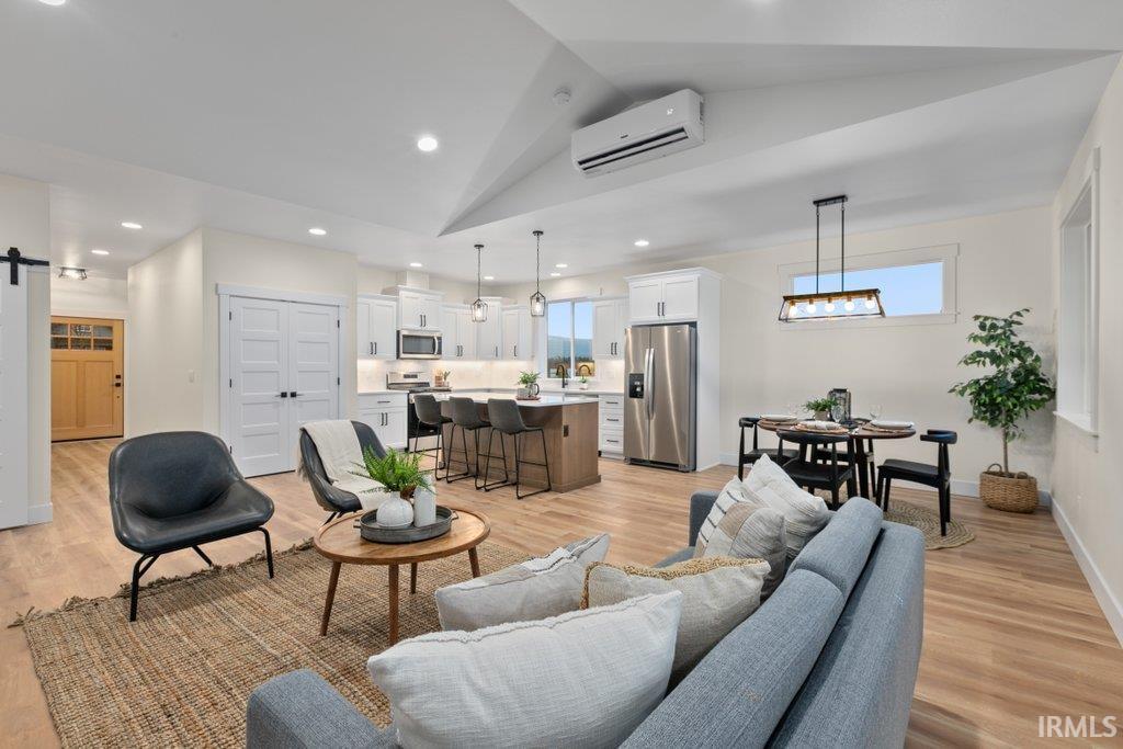 Living room featuring a barn door, light wood-style floors, lofted ceiling, plenty of natural light, and recessed lighting
