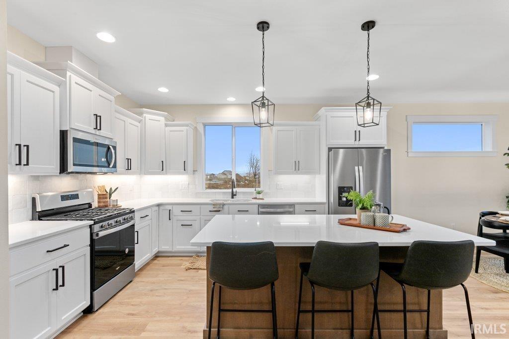 Kitchen featuring stainless steel appliances, a breakfast bar area, a kitchen island, backsplash, and light wood-style floors