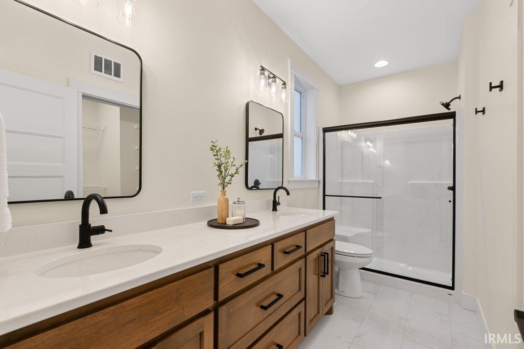 Bathroom featuring double vanity, a shower stall, and light marble finish flooring