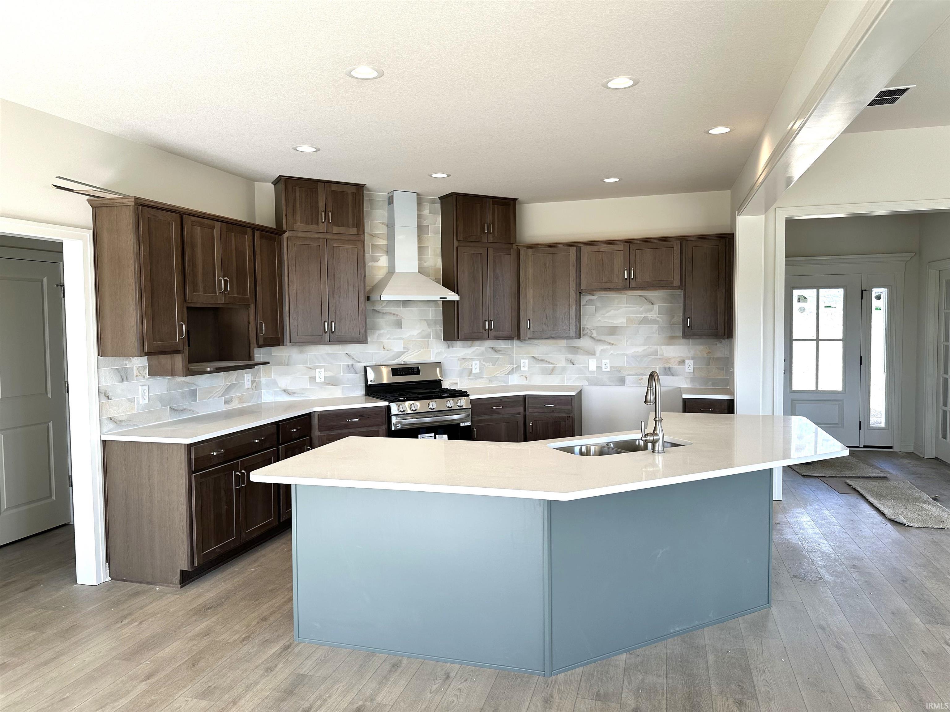 Kitchen with stainless steel range with gas stovetop, light stone countertops, dark wood finish cabinets, light wood finished floors, and a center island with sink