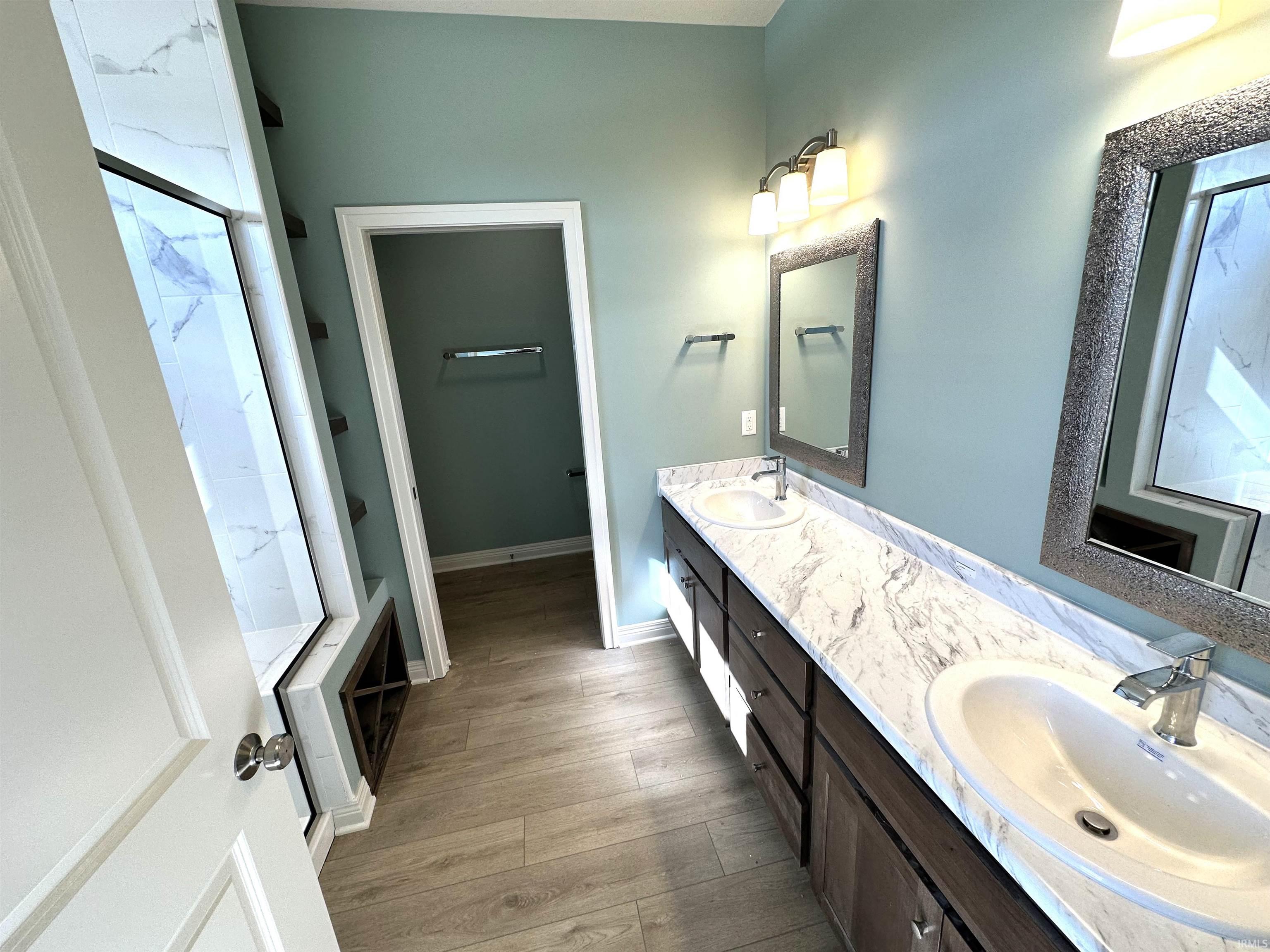 Bathroom with double vanity, light wood-style floors, and a stall shower