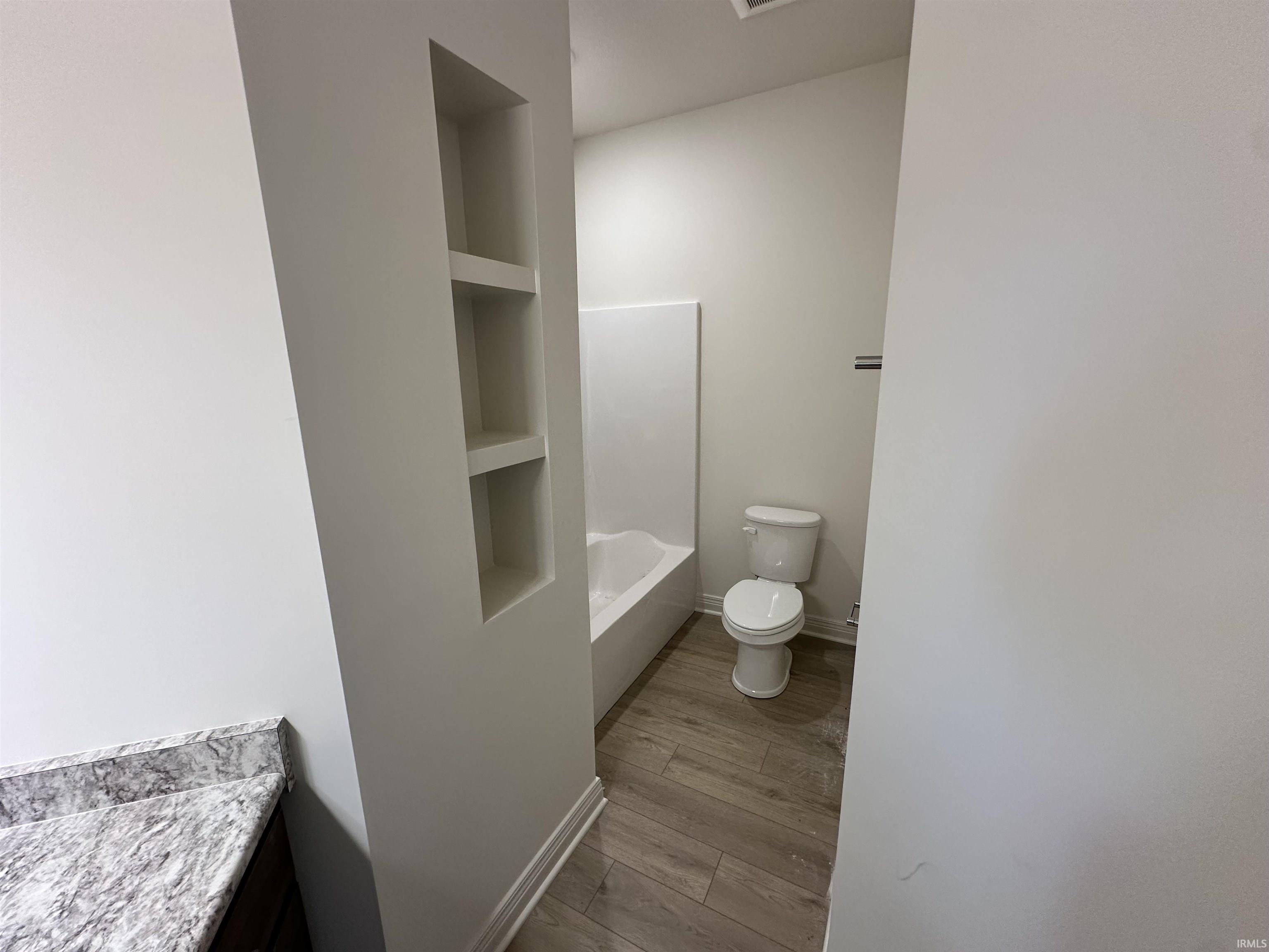Full bathroom with built in shelves, light wood-style flooring, and vanity