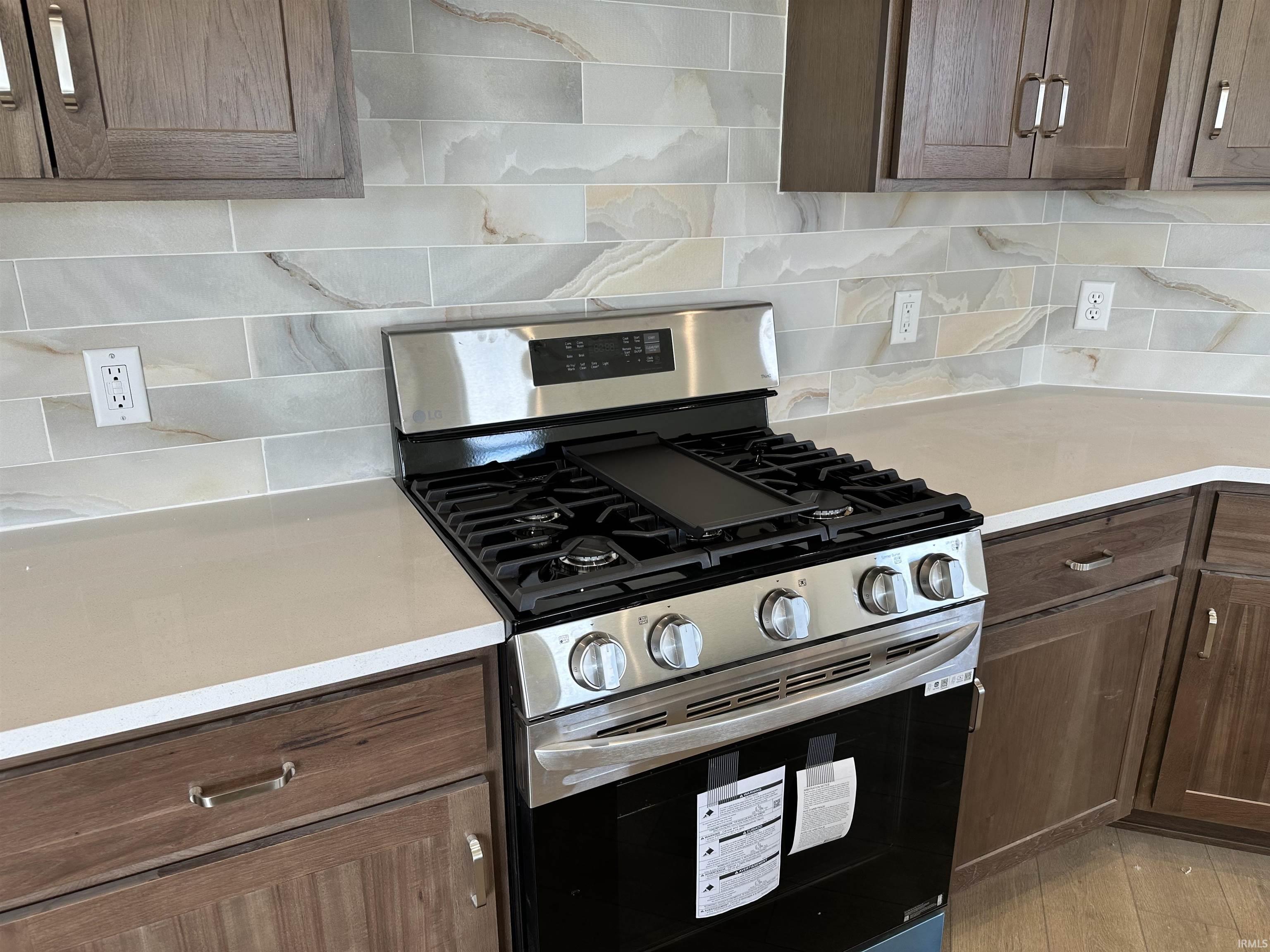 Kitchen featuring stainless steel gas stove, dark wood finish cabinets, backsplash, and light stone countertops