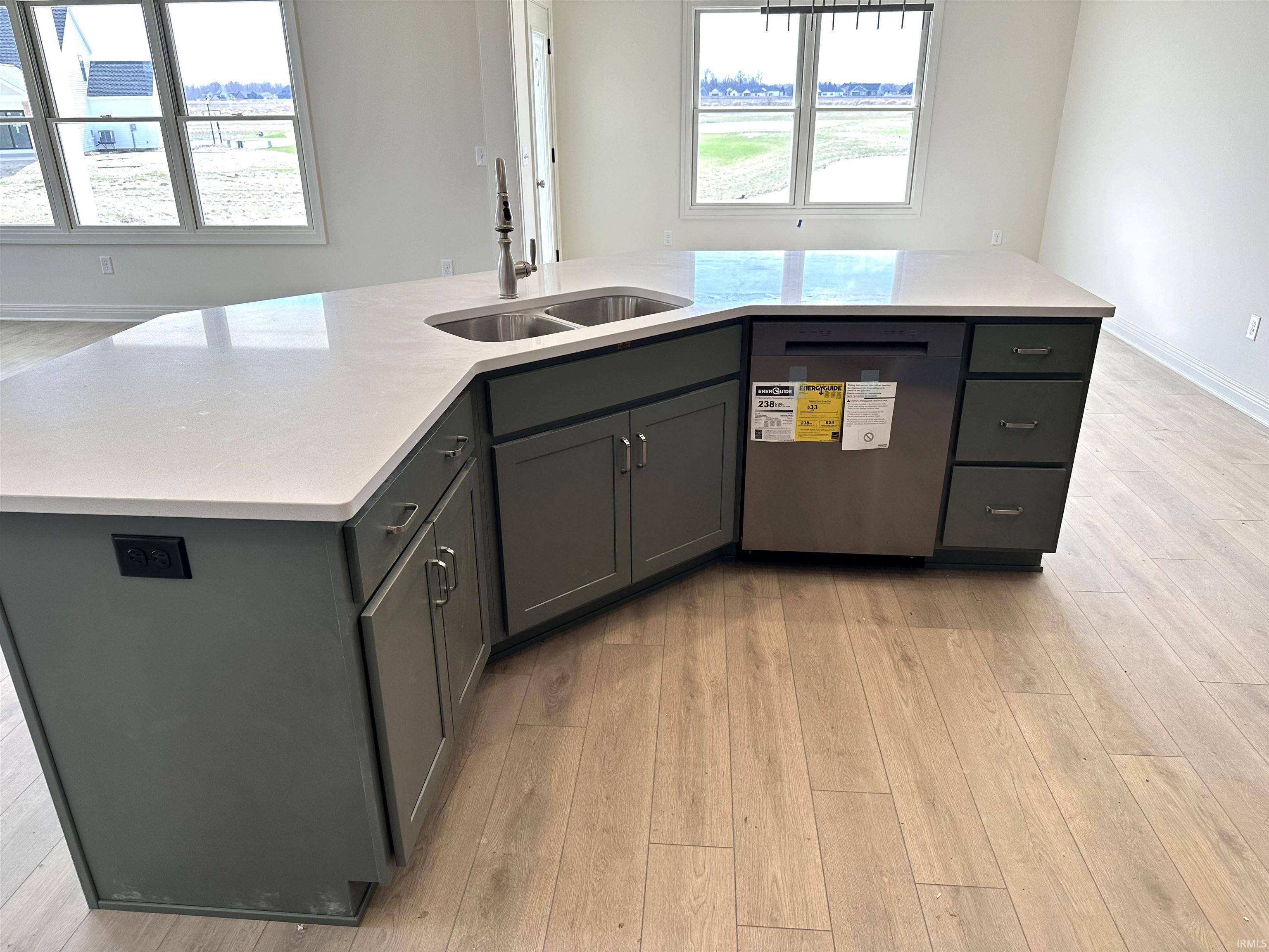 Kitchen featuring an island with sink, stainless steel dishwasher, light wood-type flooring, and gray cabinets