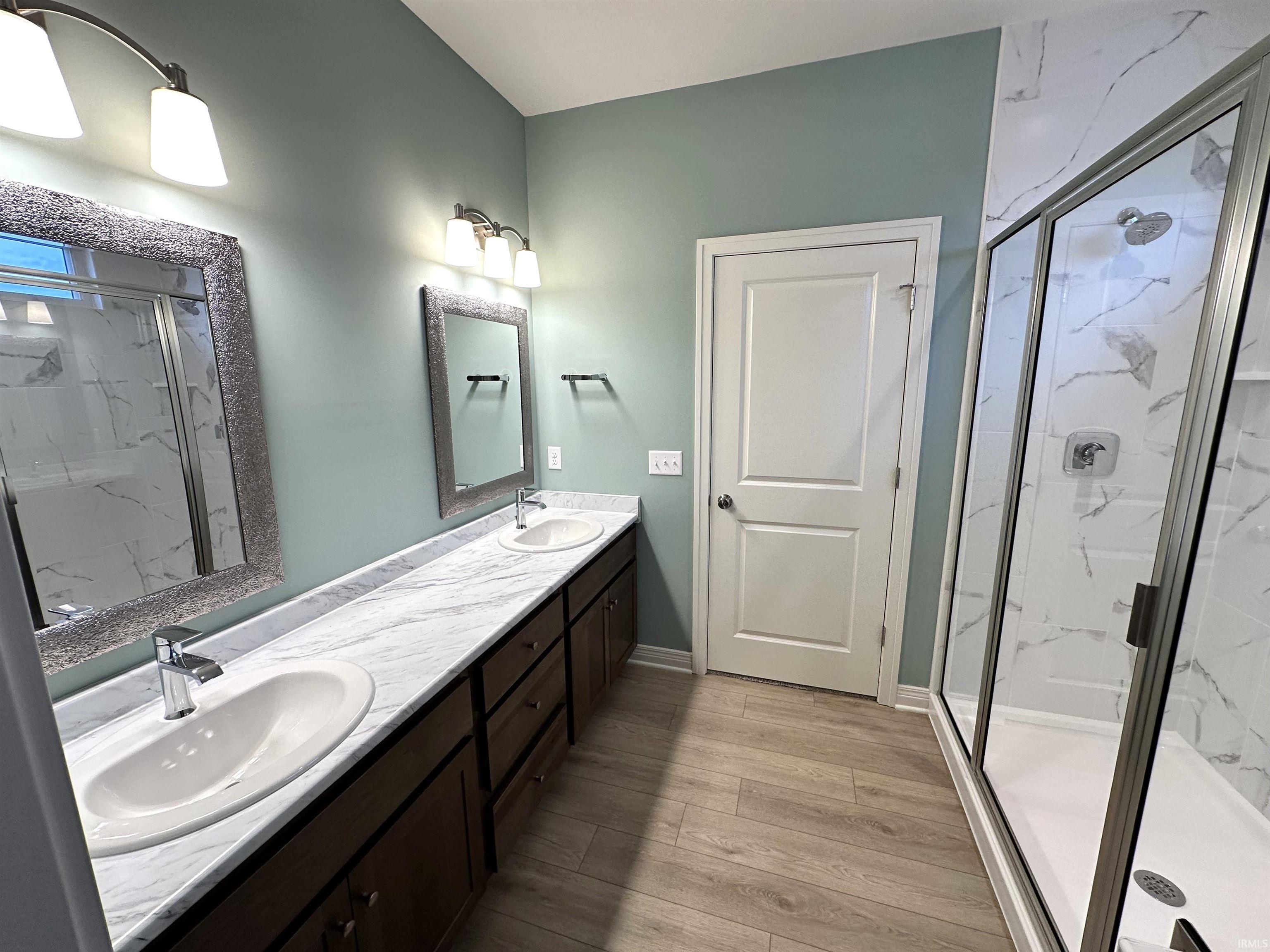 Full bathroom with a marble finish shower, double vanity, and light wood-style flooring