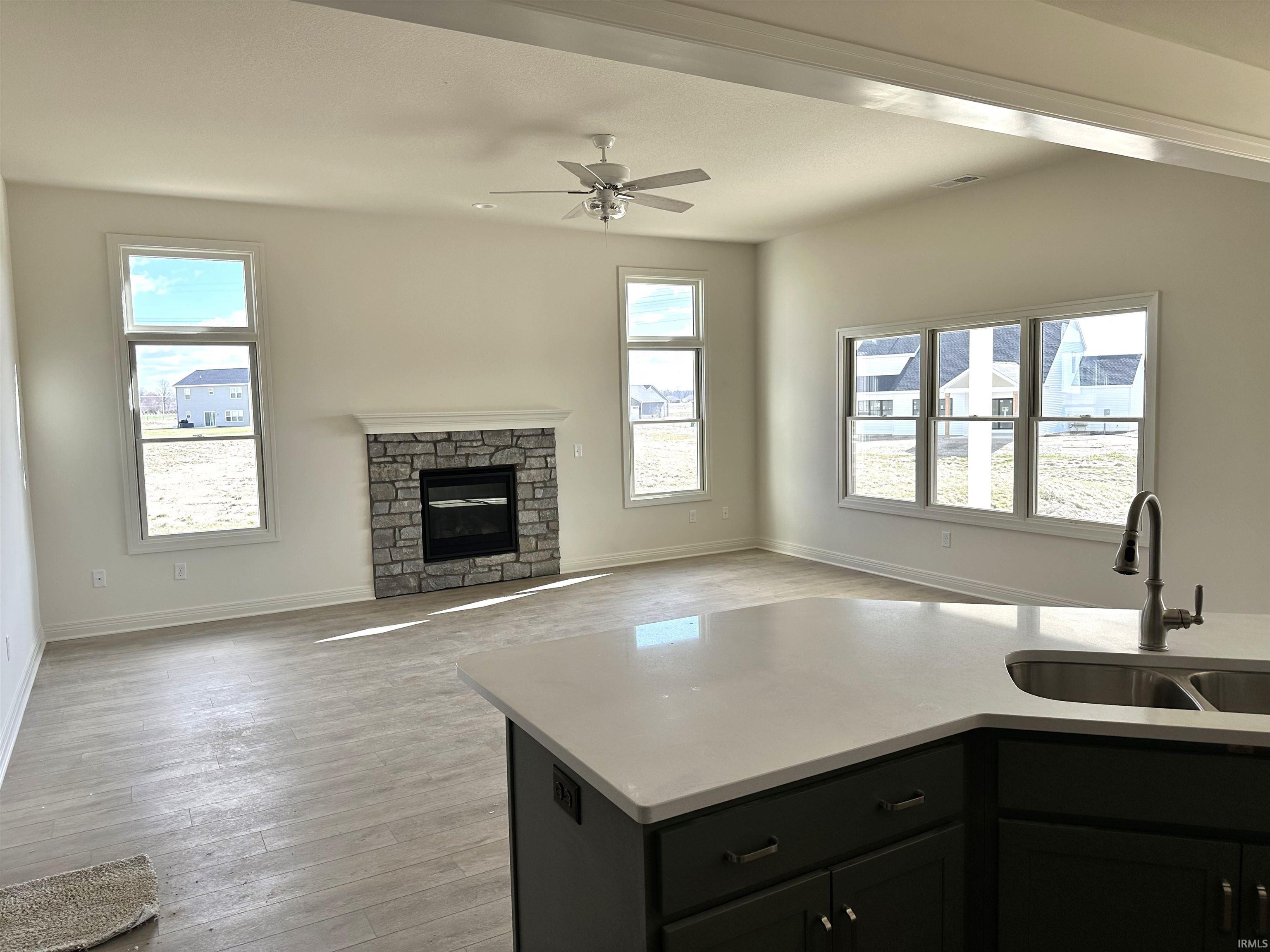 Kitchen featuring a stone fireplace, light wood-style floors, open floor plan, a ceiling fan, and light stone counters