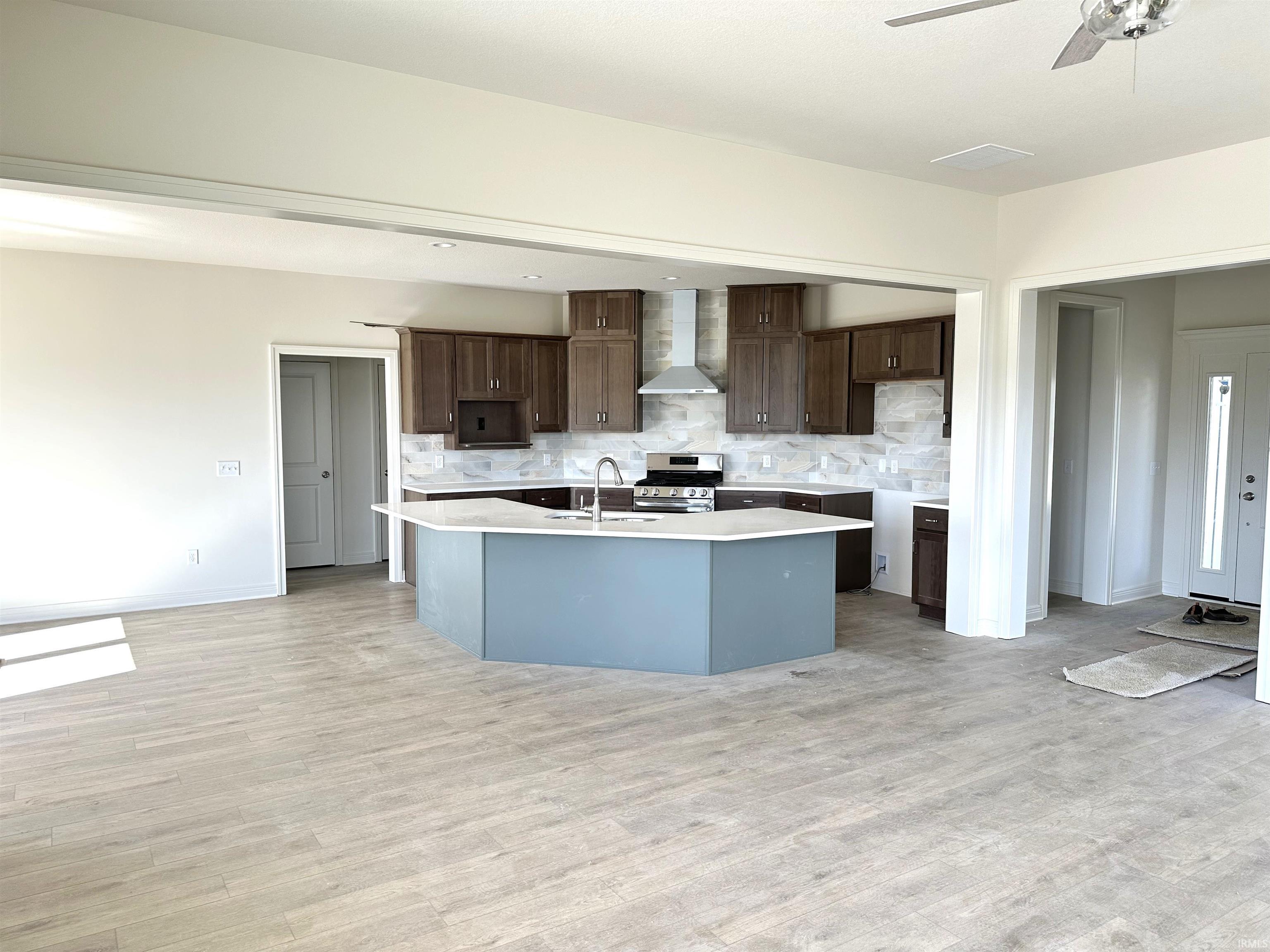 Kitchen featuring dark wood finish cabinets, decorative backsplash, stainless steel range, a kitchen island with sink, and light wood finished floors